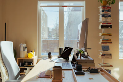 Sunlit home office desk with computer and books.