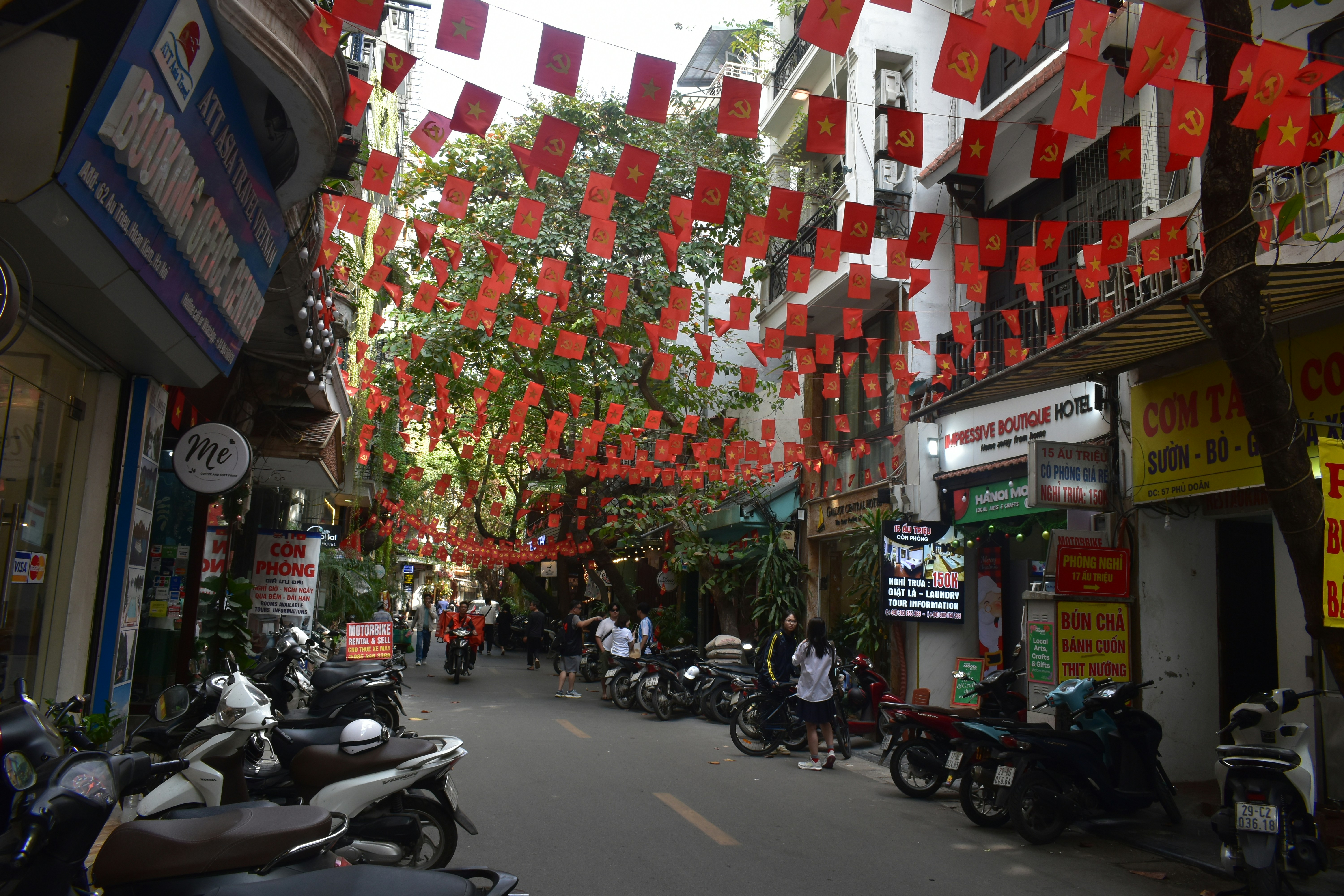 Street decorated with red flags and parked motorcycles.