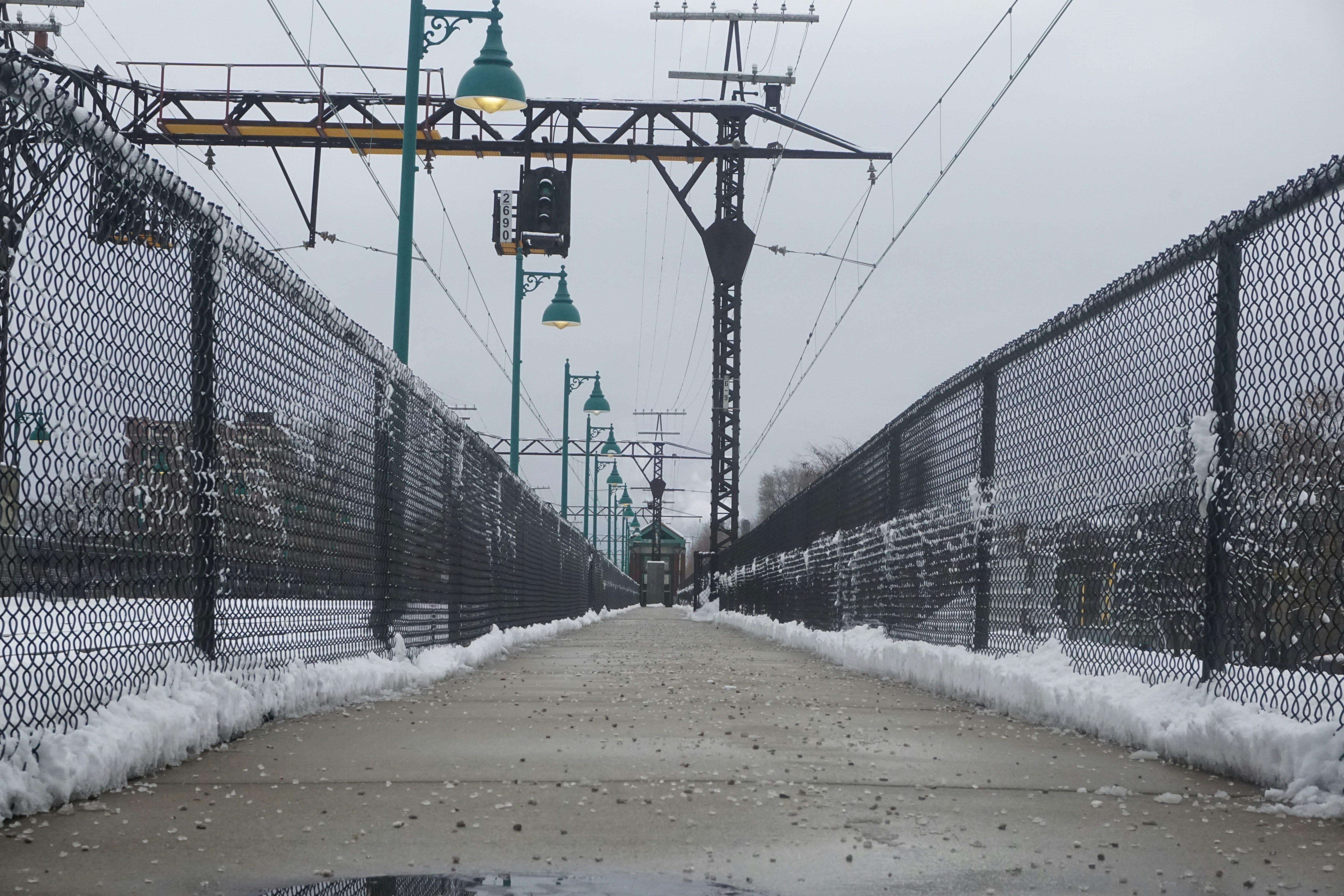Snowy path with fences and streetlights under sky