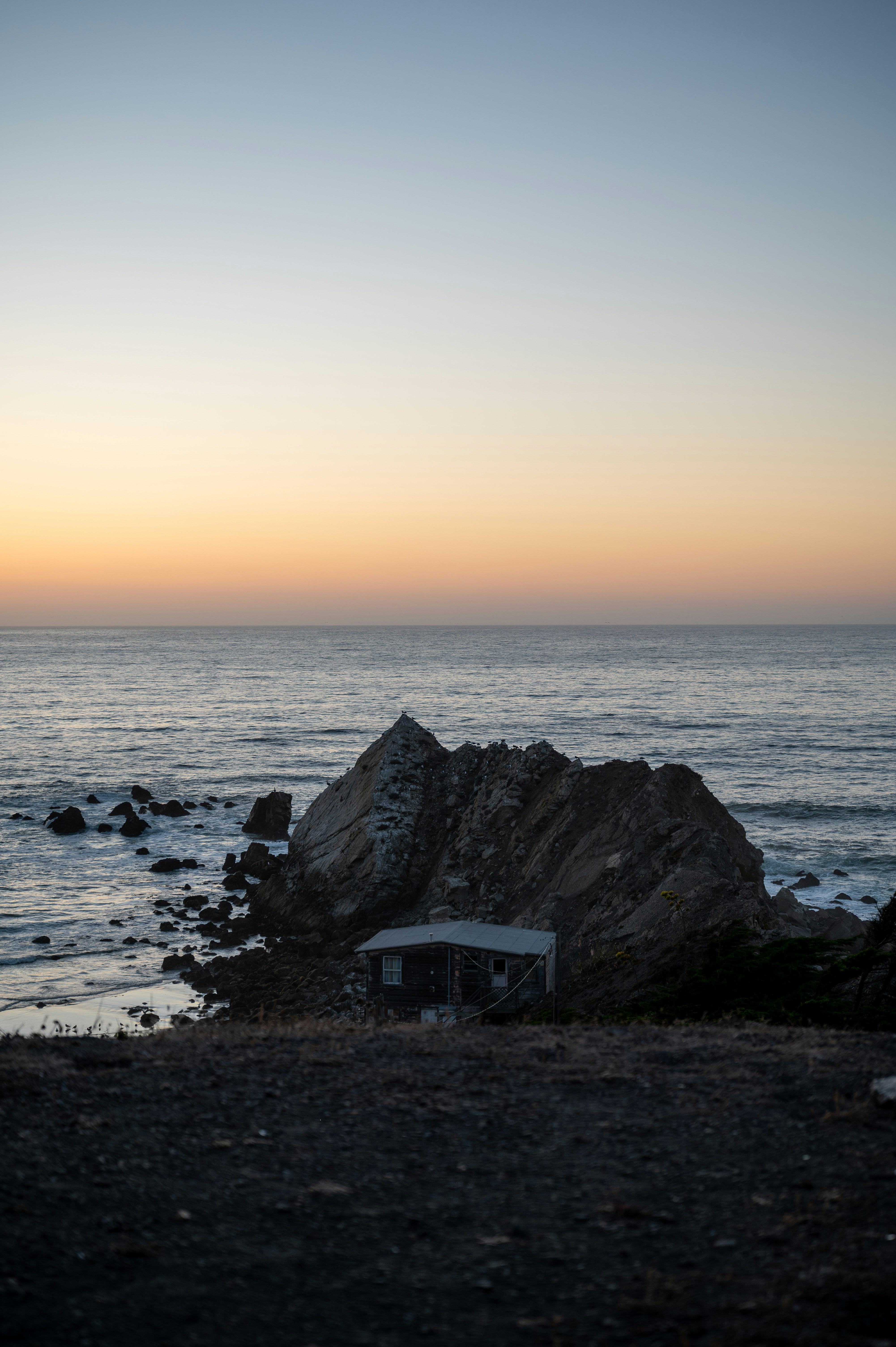 Small shack nestled by a large rock on the coast.