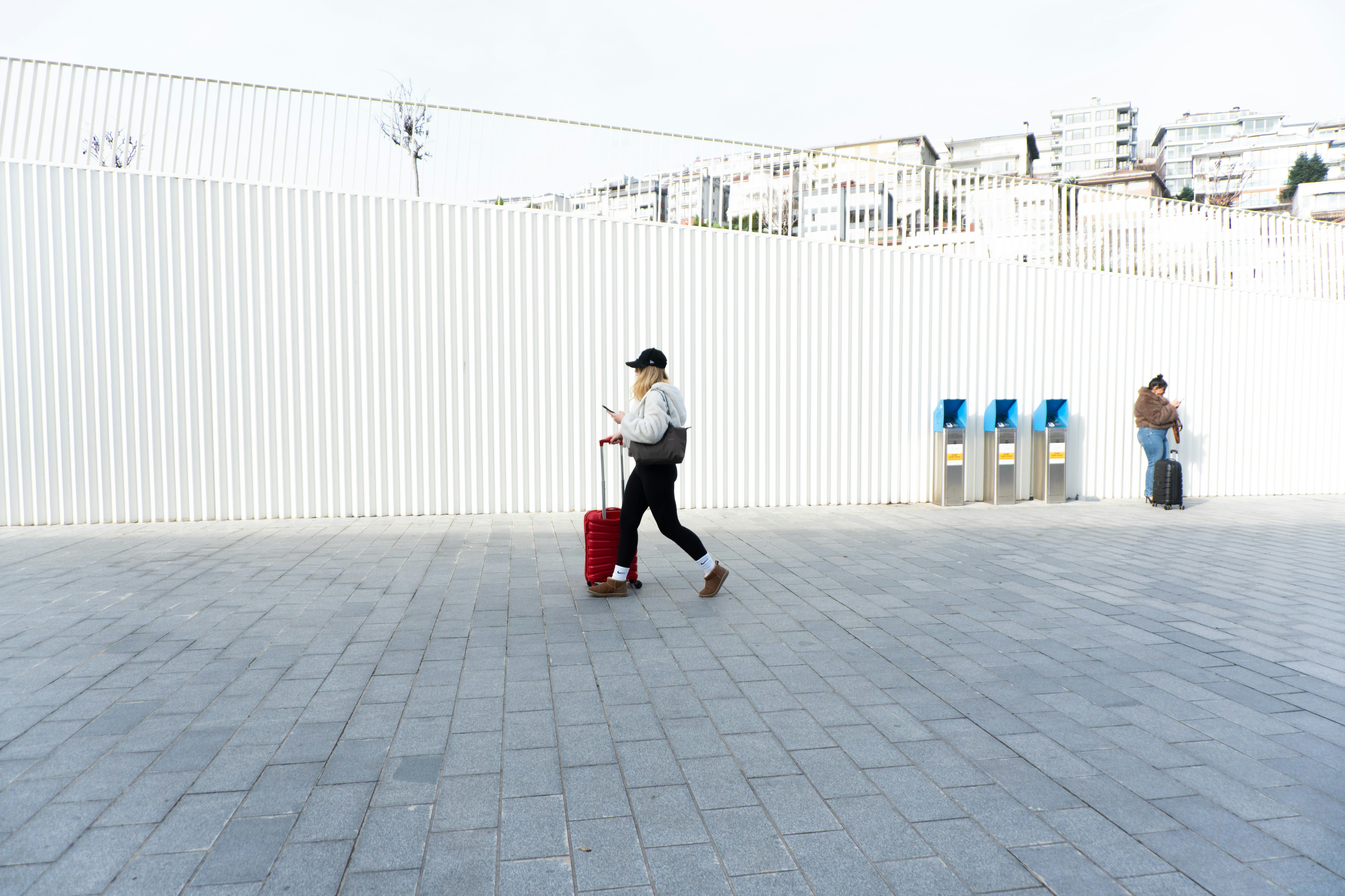 Person with red suitcase walks past ticket machines.
