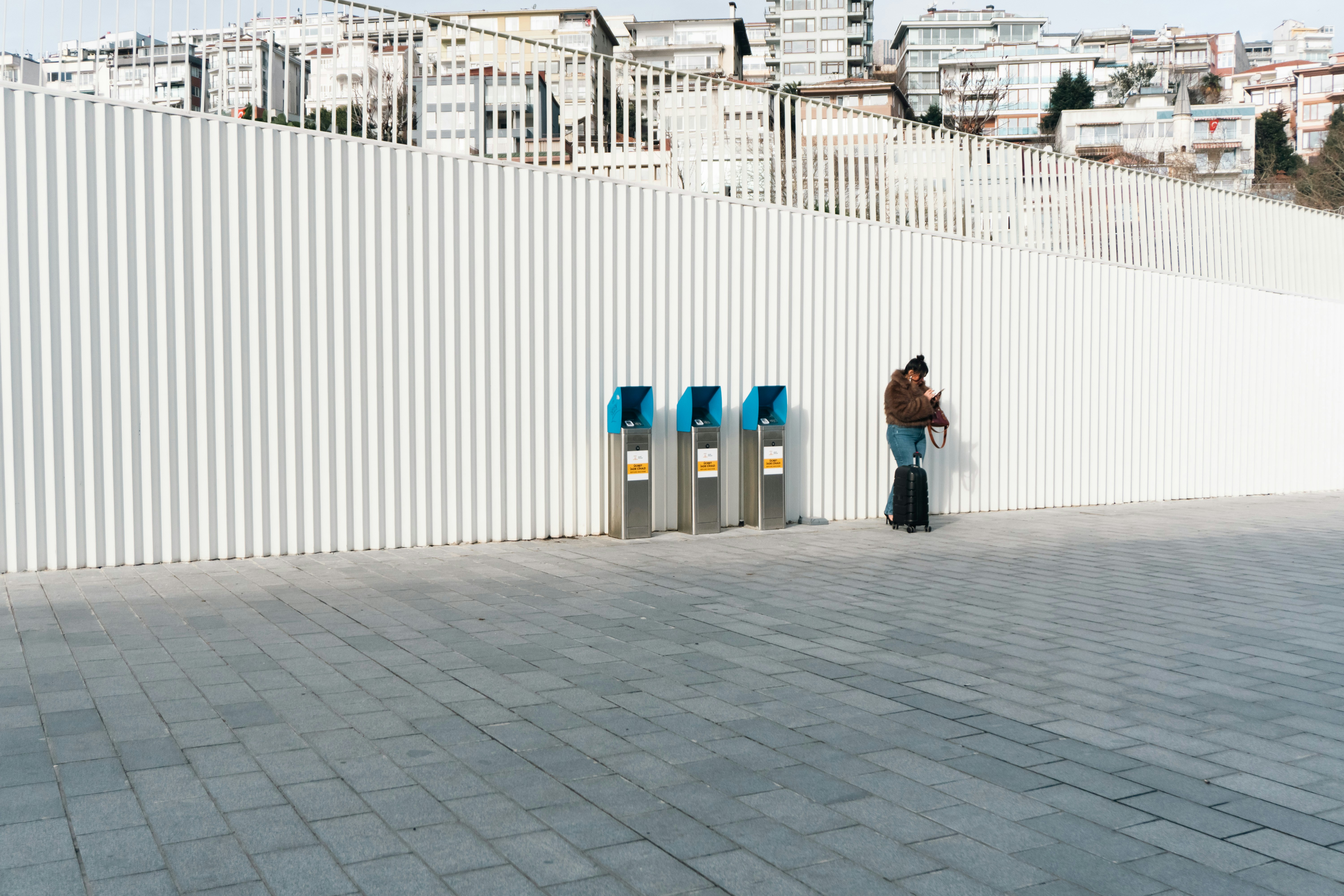 A person stands with a suitcase next to ticket machines.