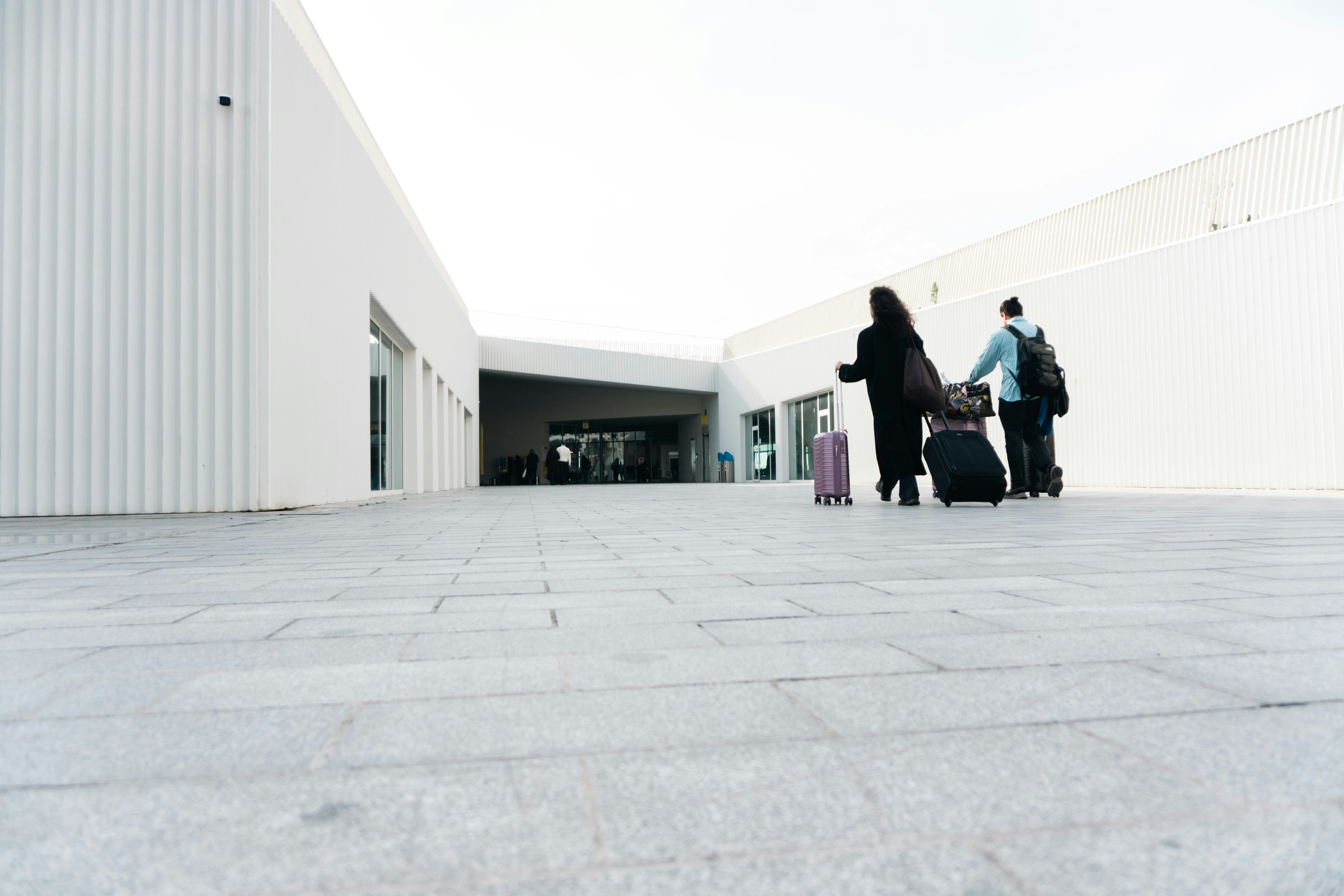 Two people with luggage walking towards a modern building.