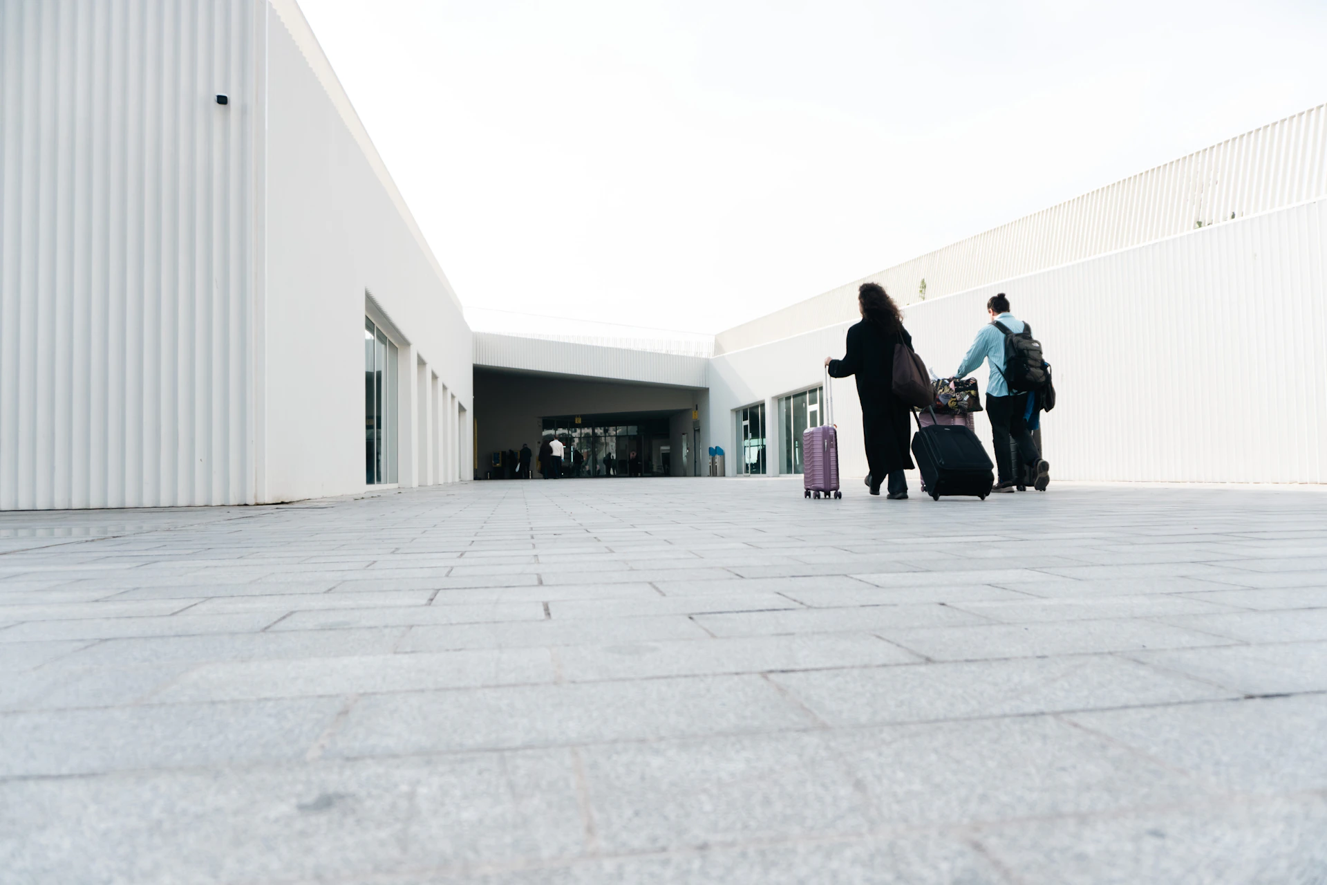 Two people with luggage walking towards a modern building.