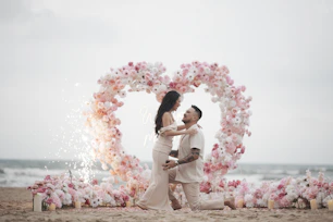 Couple embracing on beach with heart-shaped floral arch