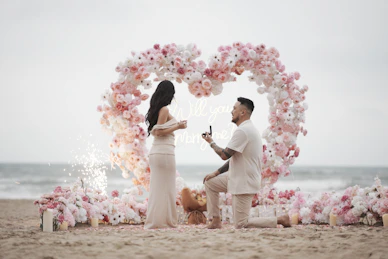Man proposes to woman on beach with heart arch.