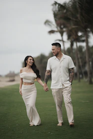A couple walks hand-in-hand on a grassy field.