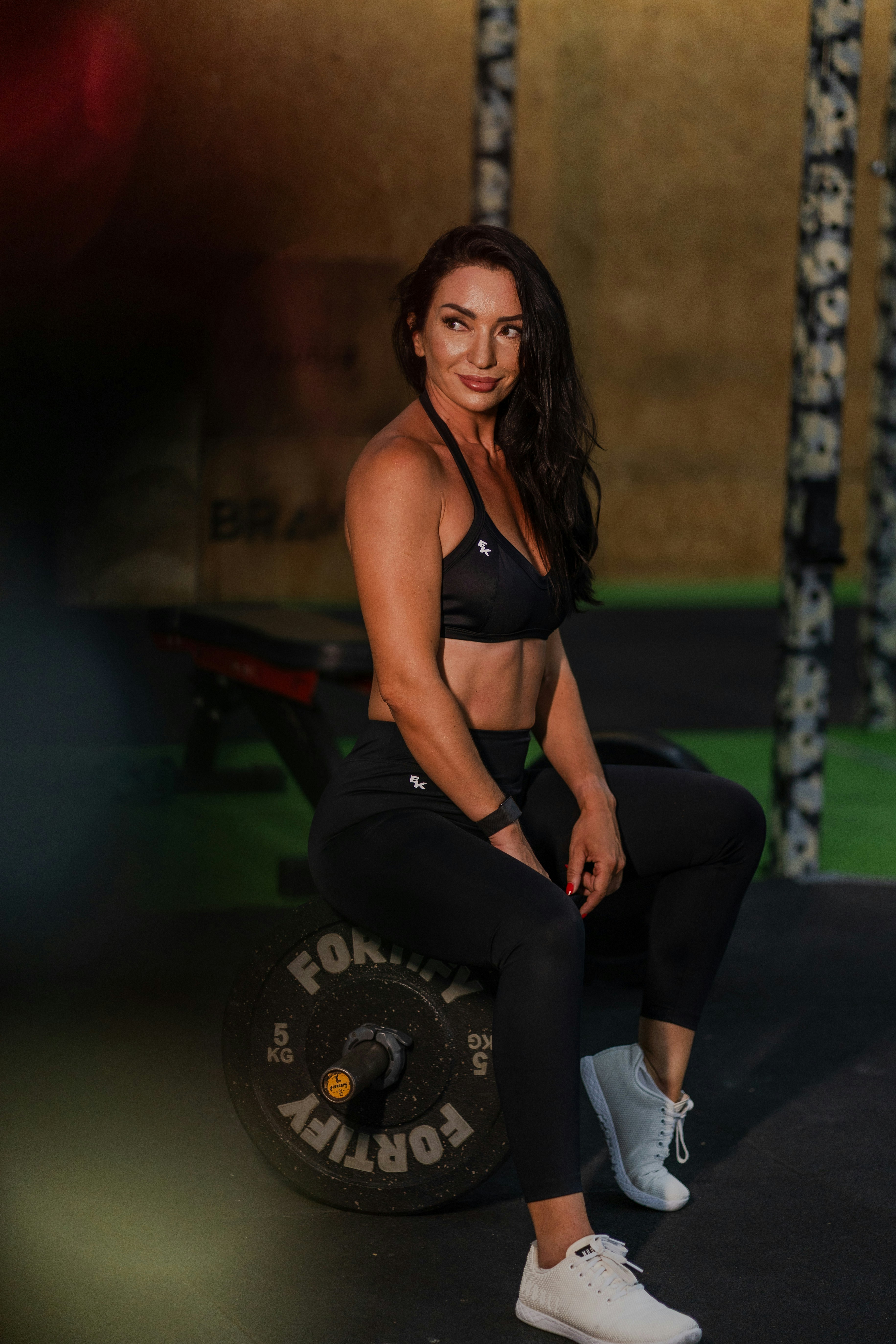 A woman in athletic wear sits on a weight plate.