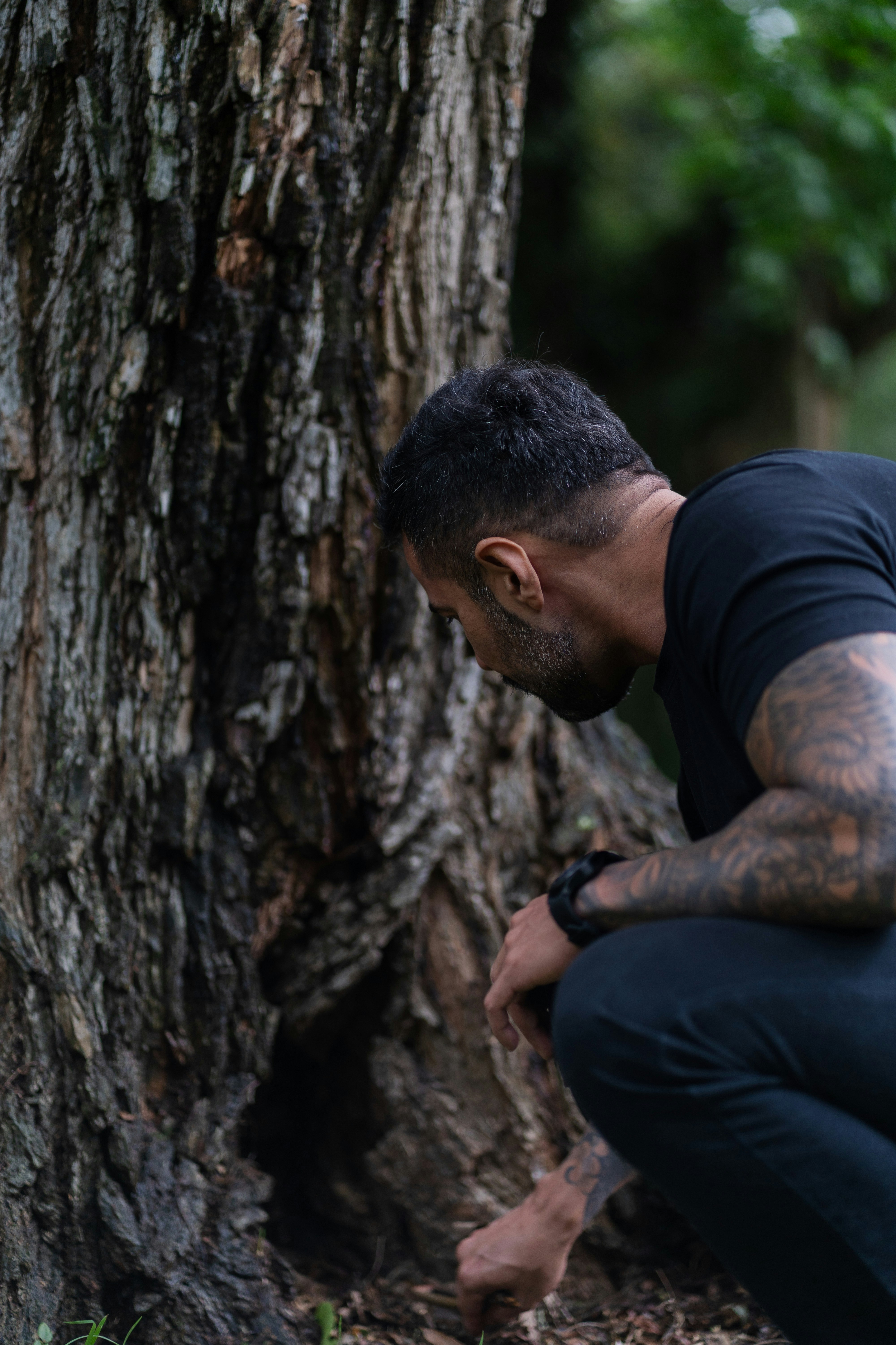 Man crouching by a large tree trunk