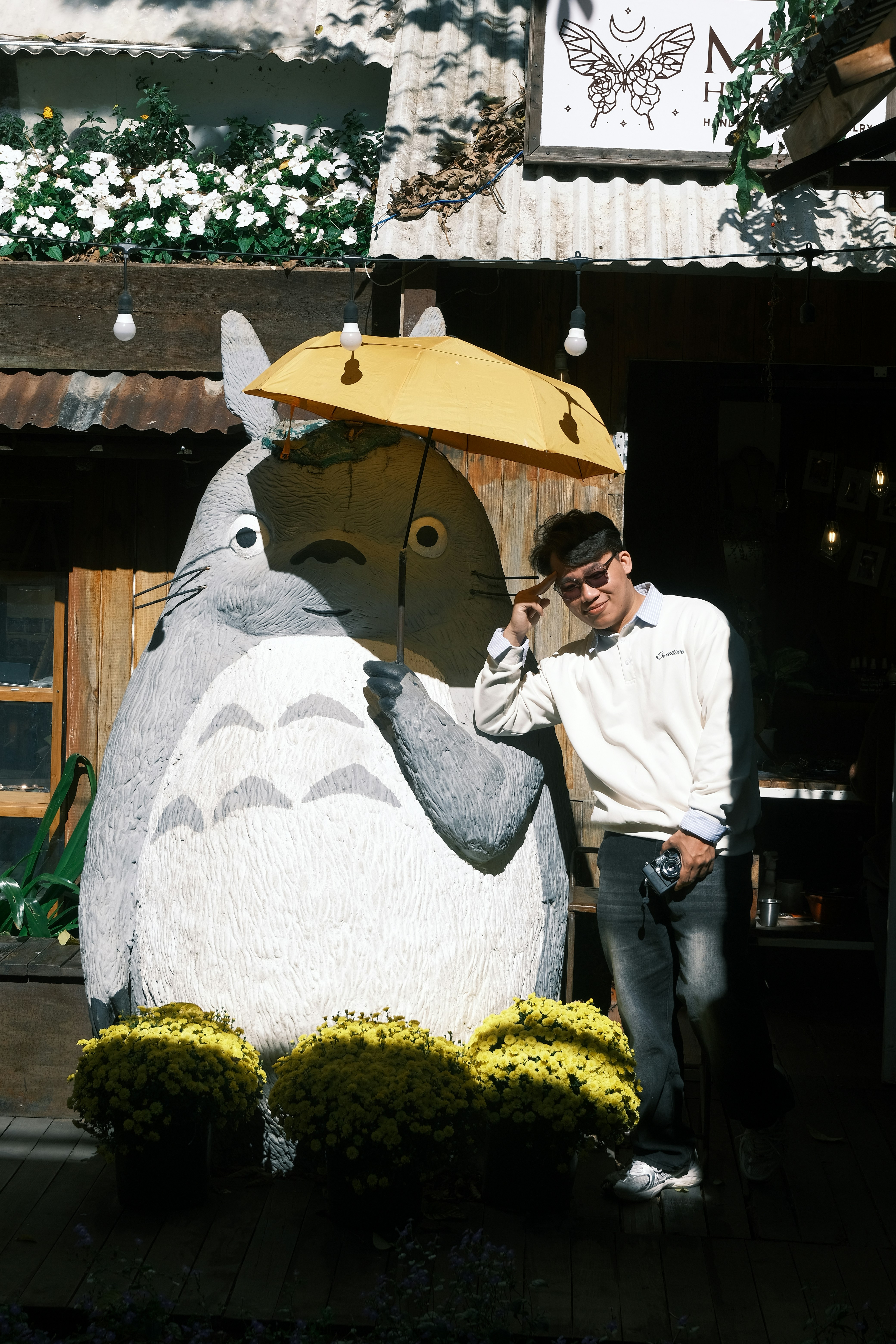 Hombre posando con una gran estatua de totoro sosteniendo un paraguas