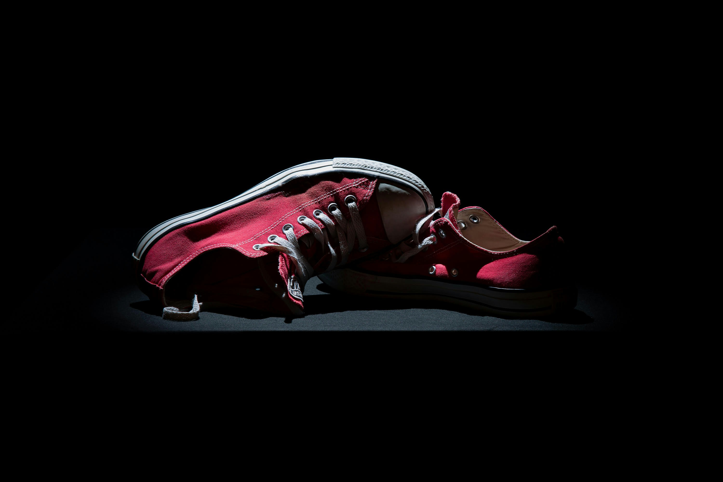 A single red sneaker lies on a dark surface.