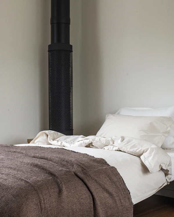 A made bed with a brown wool blanket over white linen