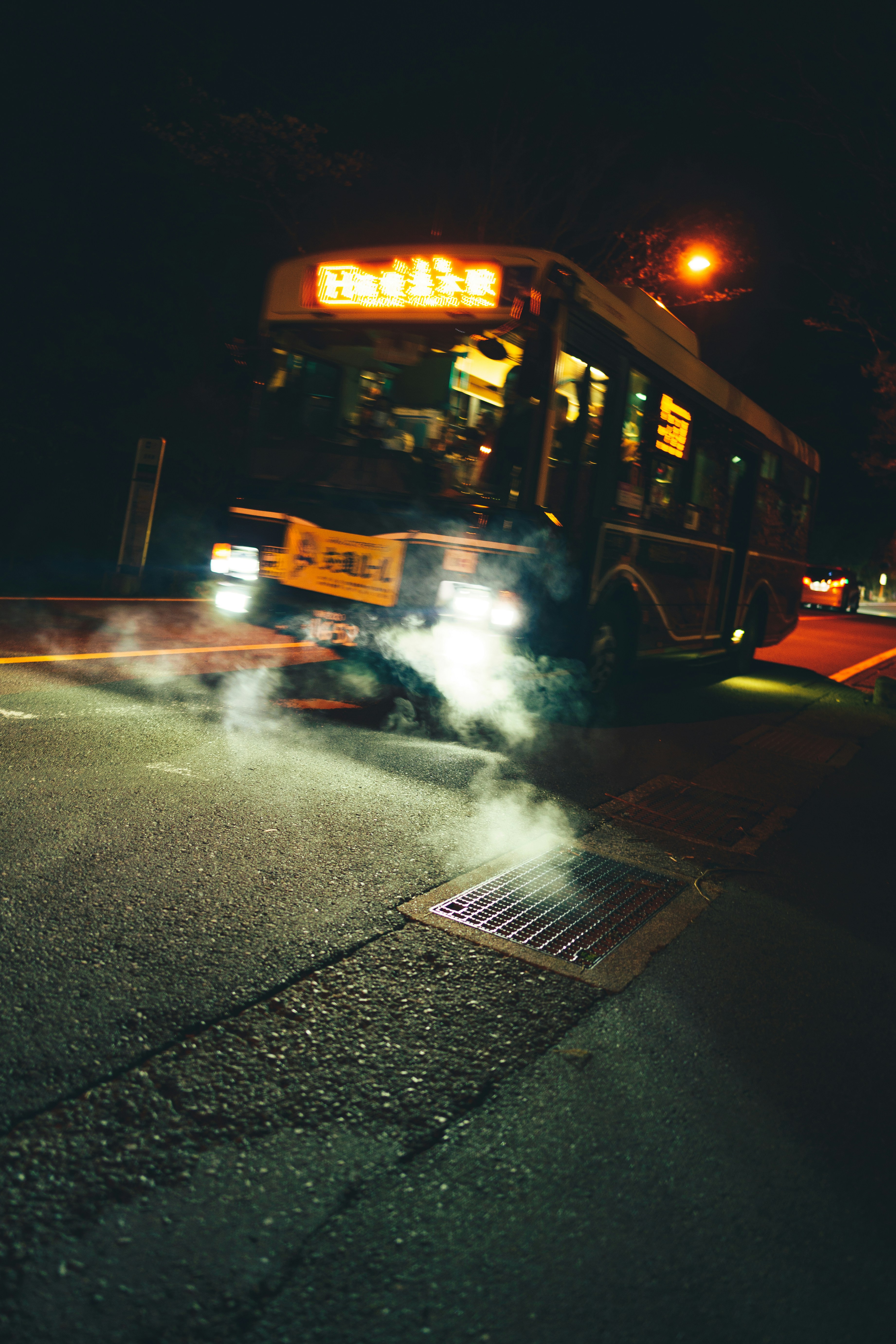 Bus emitting steam at night on a street.