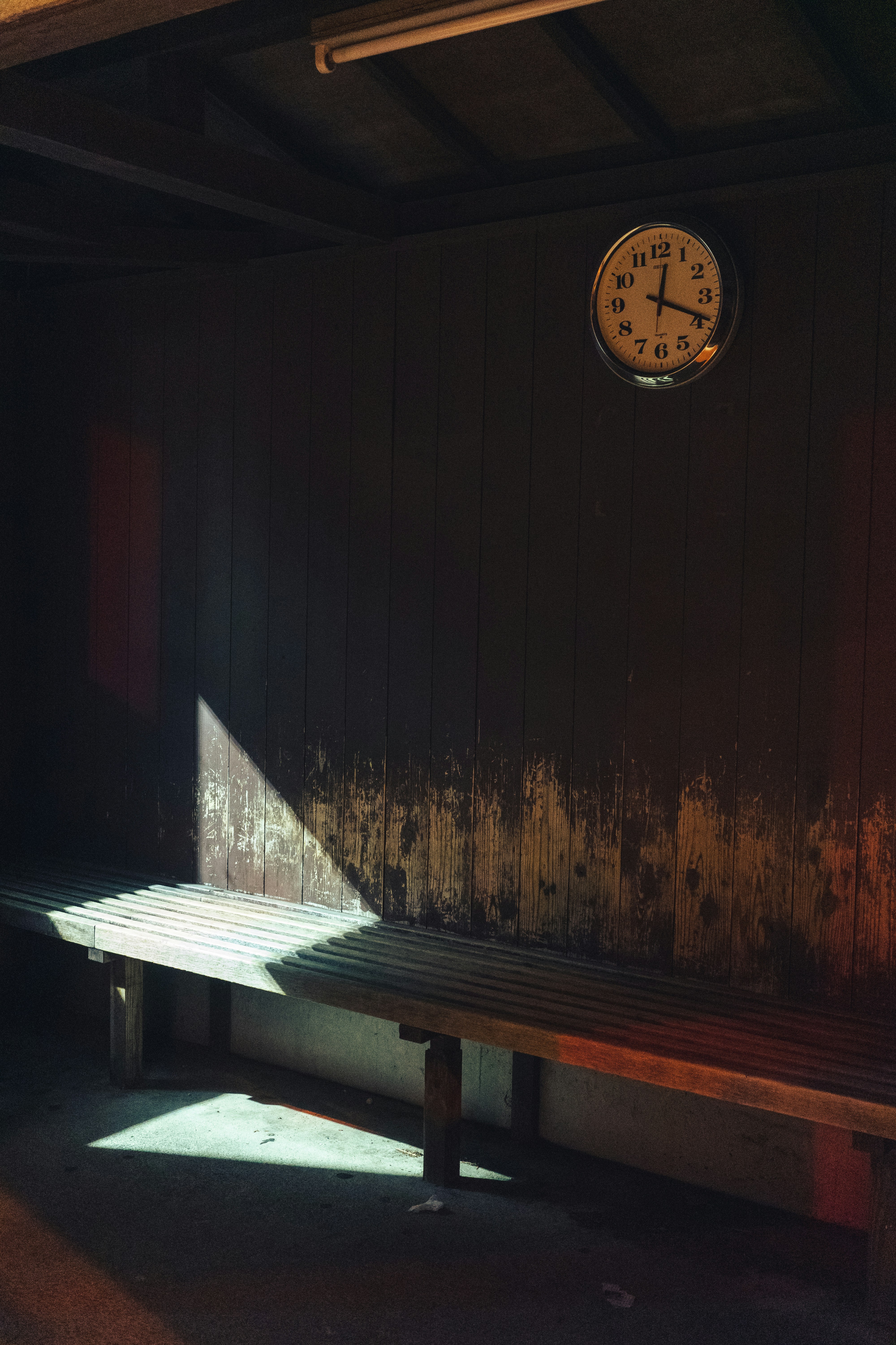 A clock hangs above a wooden bench with sunlight.