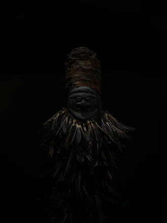 A dark tribal mask with feathers against black background
