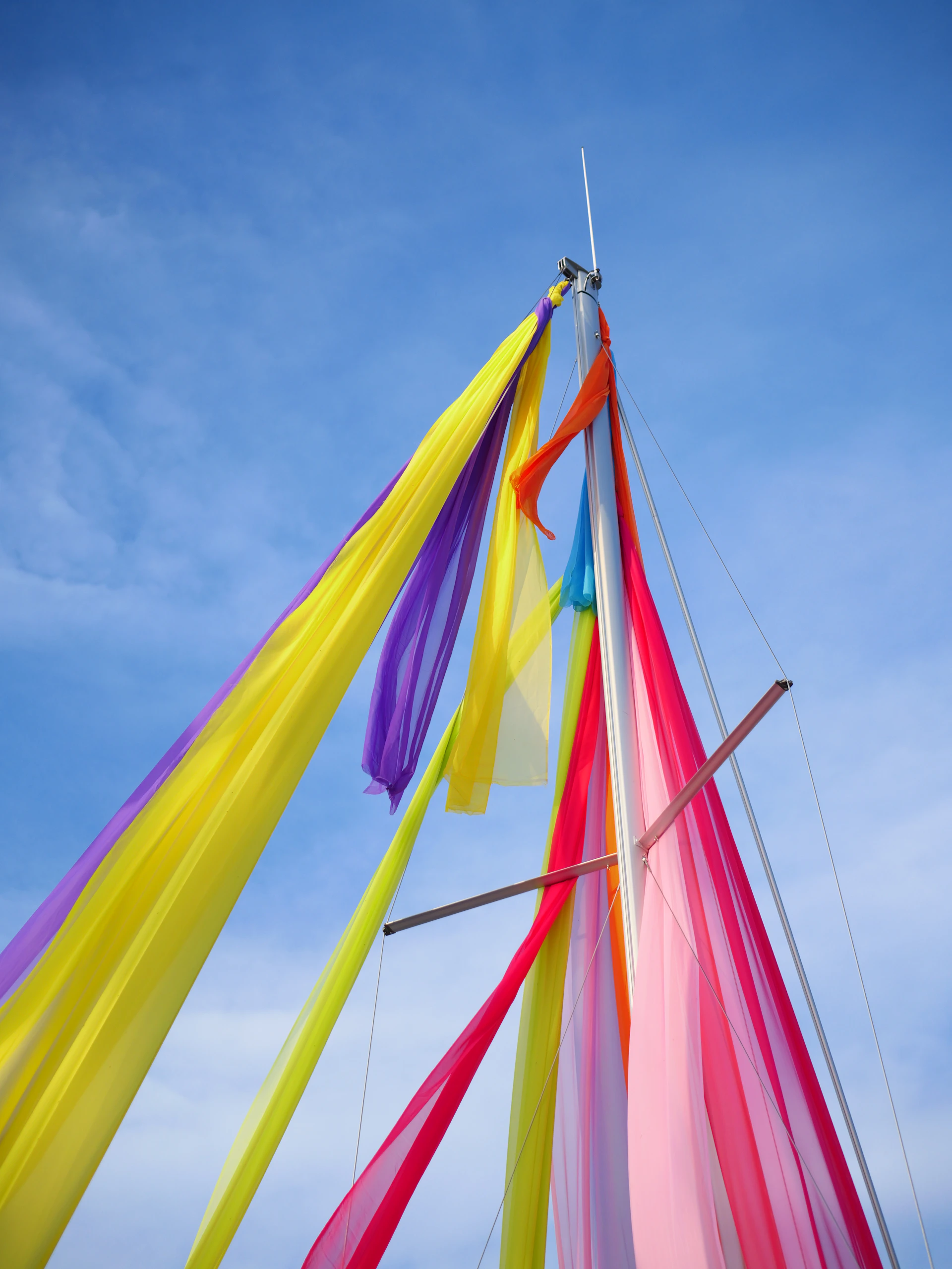 Colorful streamers adorn a sailboat mast against a blue sky