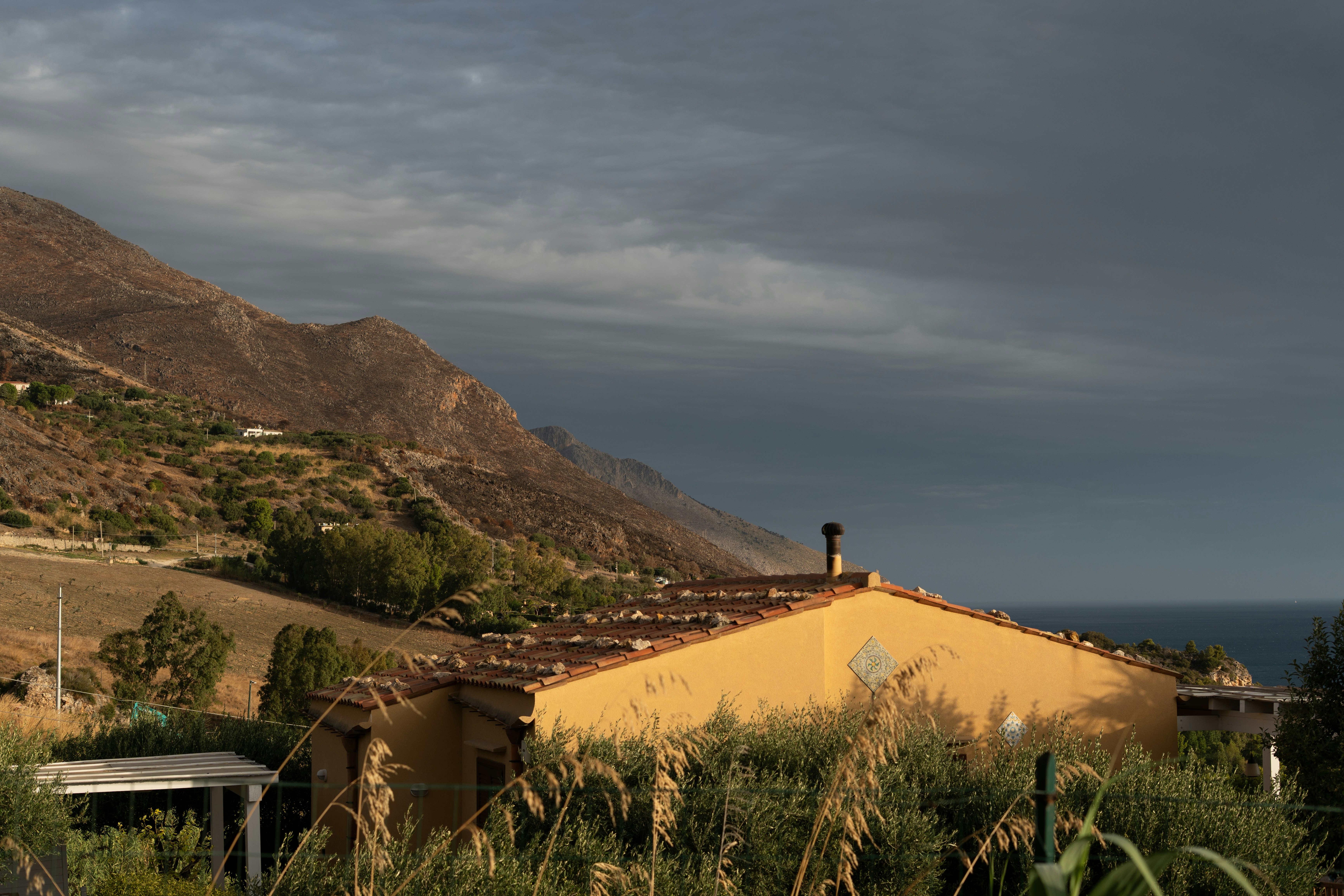 A yellow house sits on a hill overlooking the ocean.