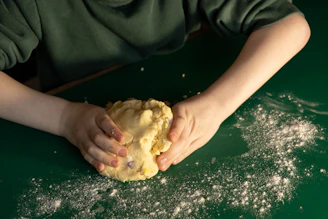 Child's hands kneading dough on a green surface.