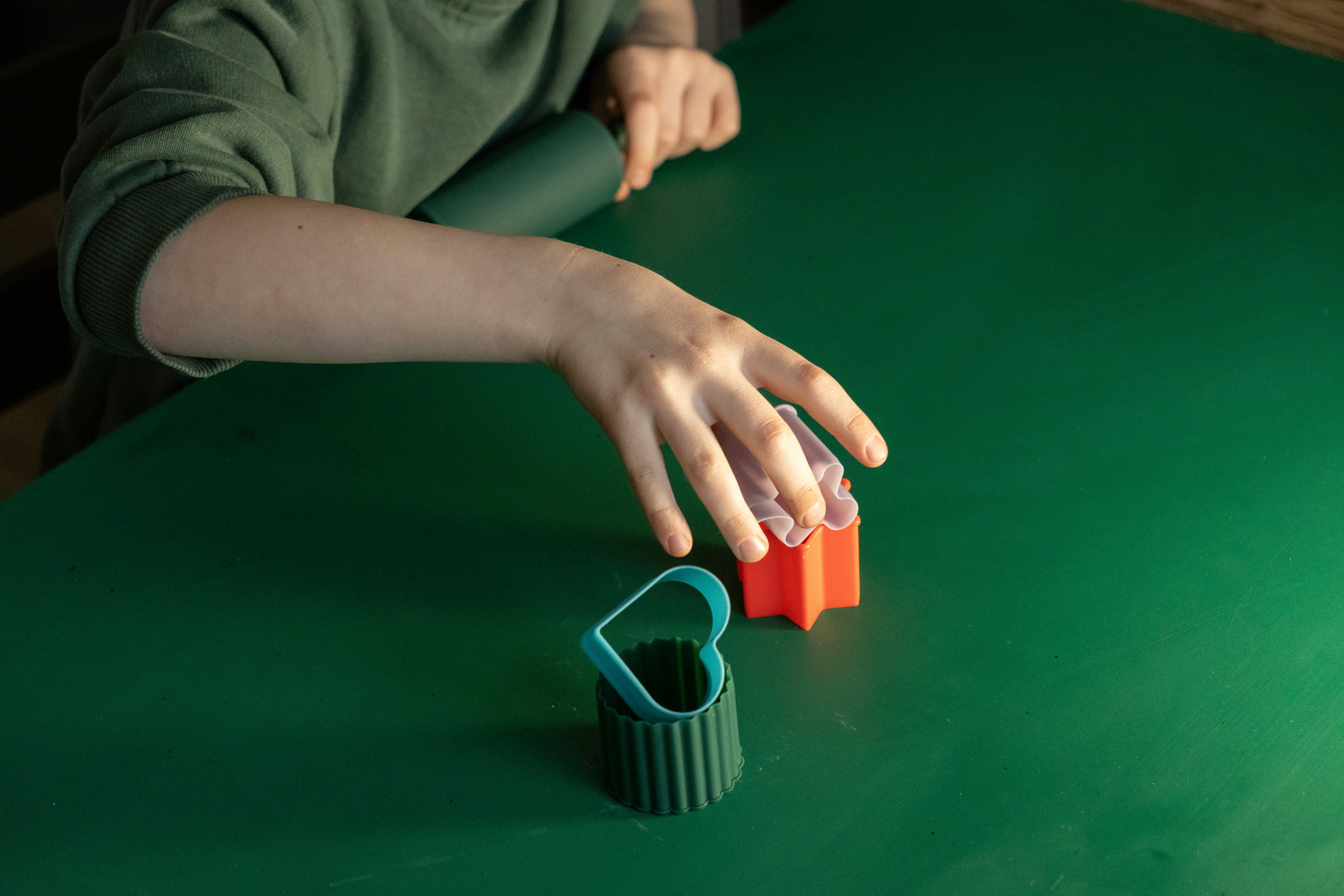 Mani di bambini che giocano con le tagliabiscotti su un tavolo verde