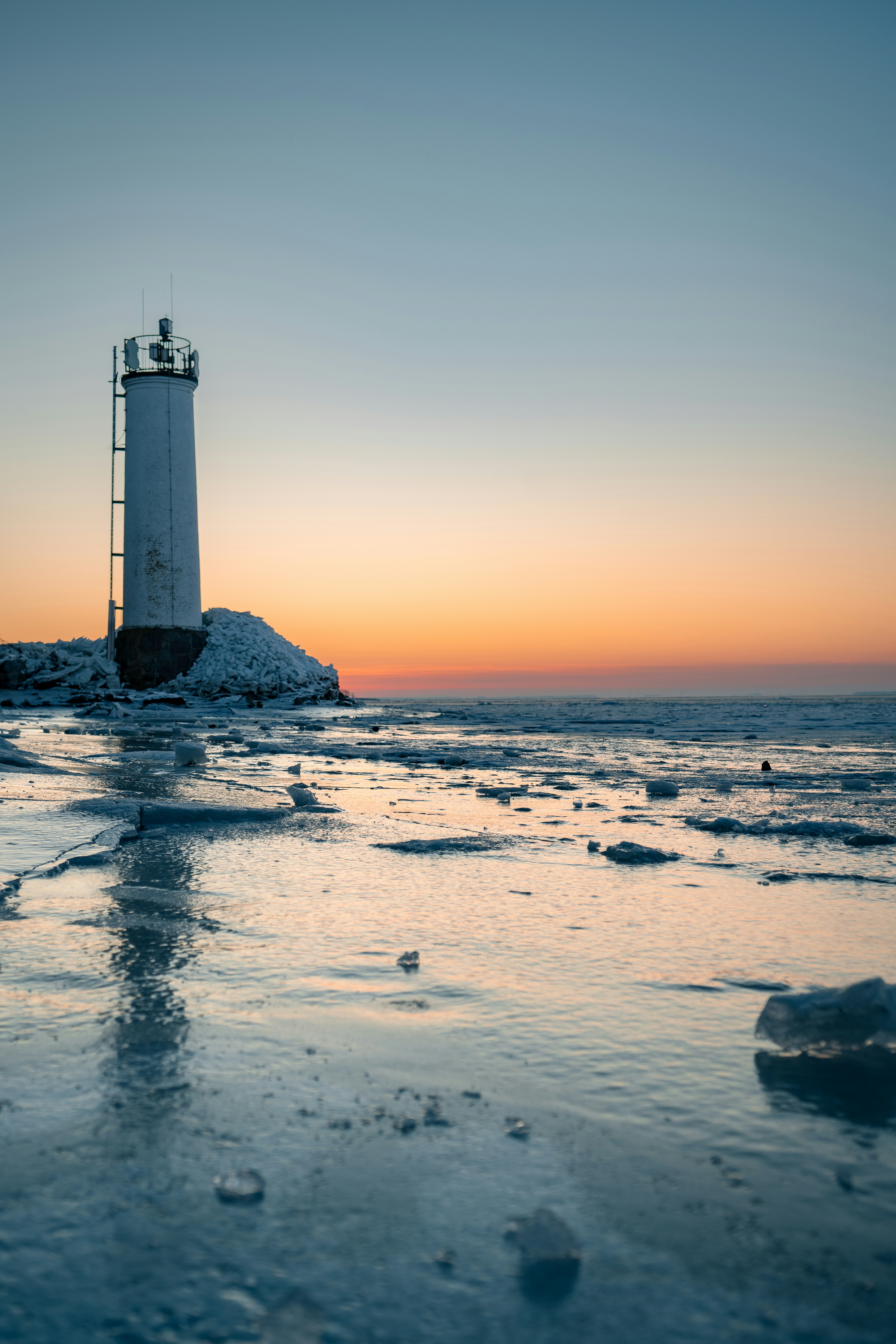 White lighthouse on a frozen shore at sunset