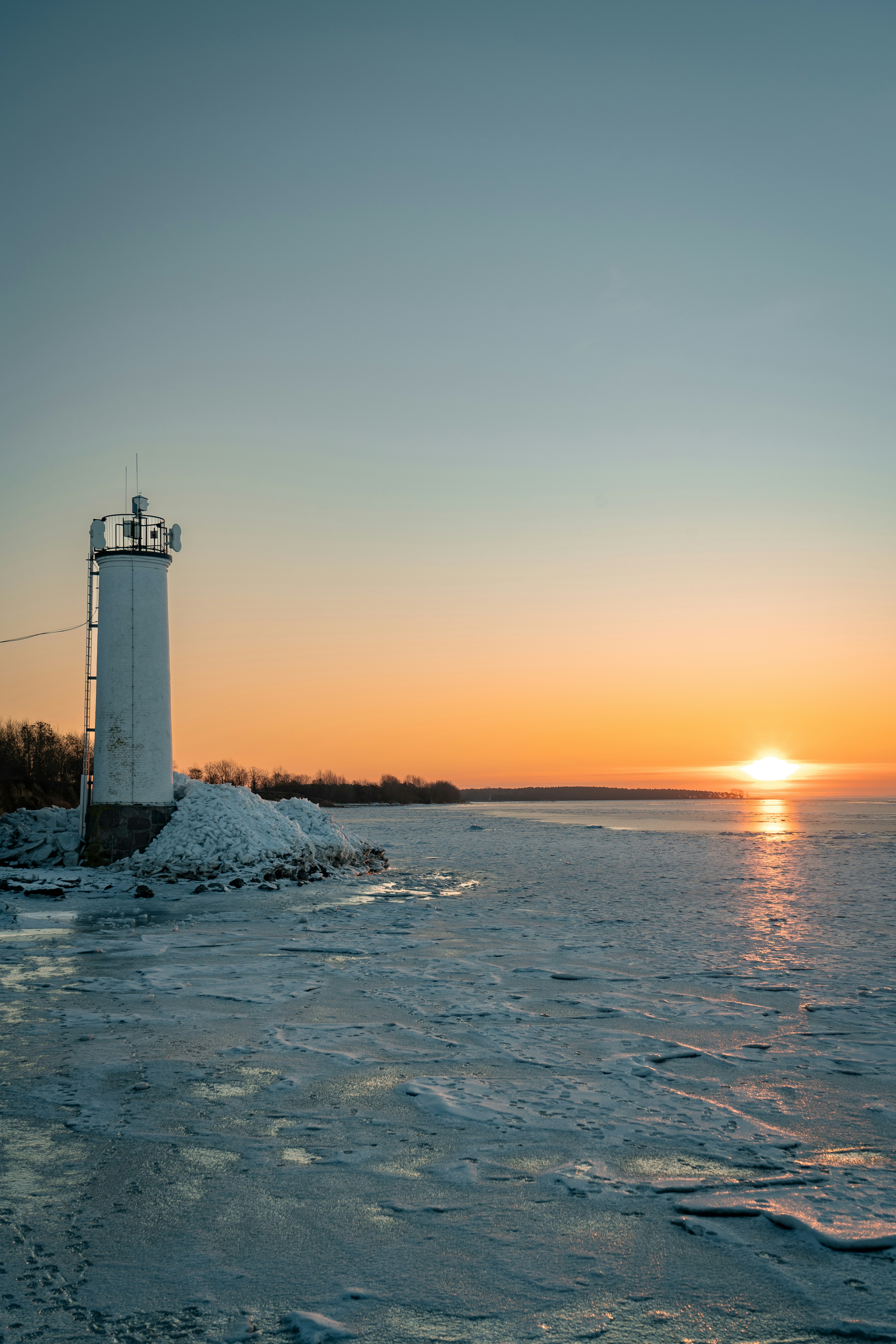 White lighthouse on a frozen coast at sunset.