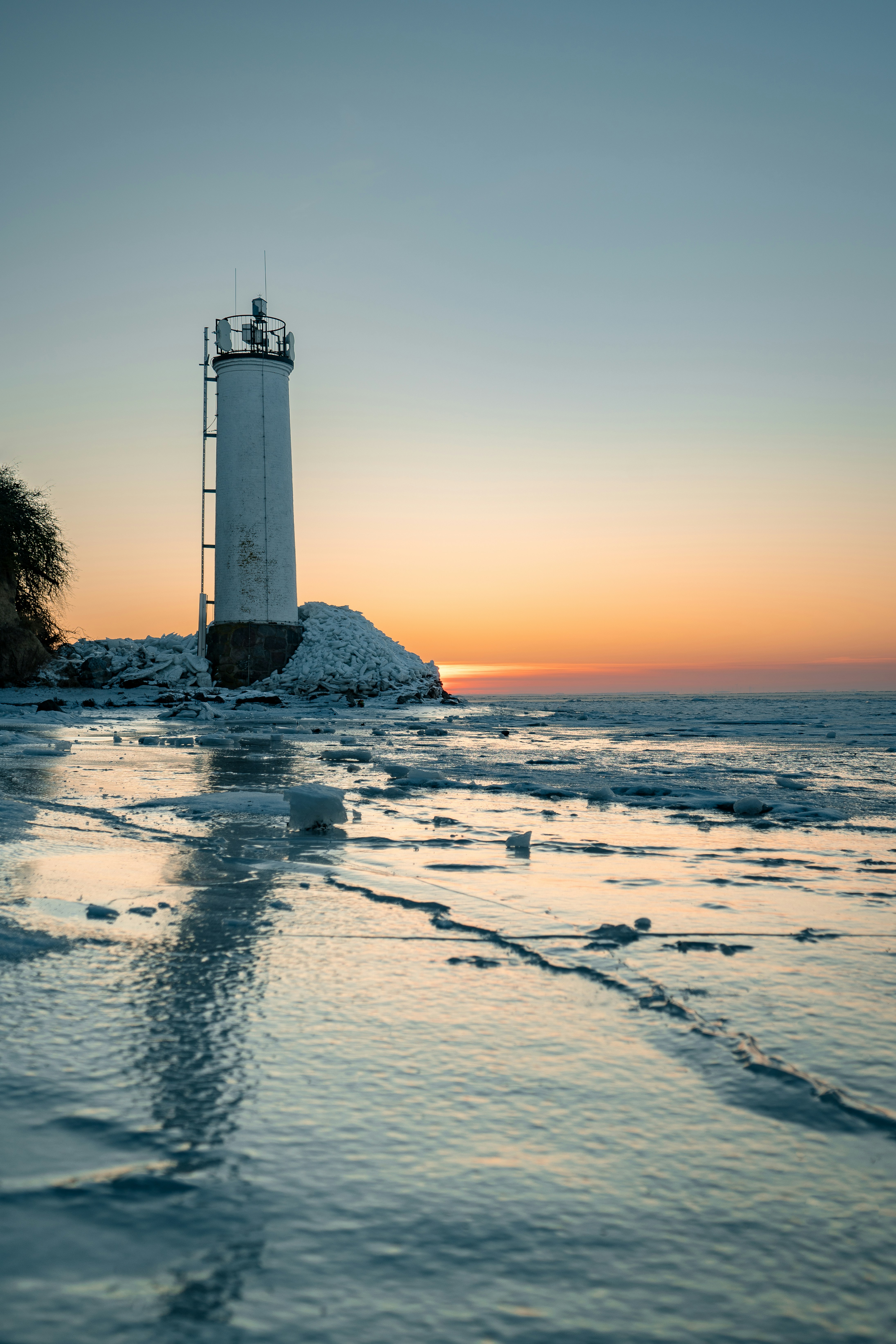 White lighthouse on a frozen shore at sunset