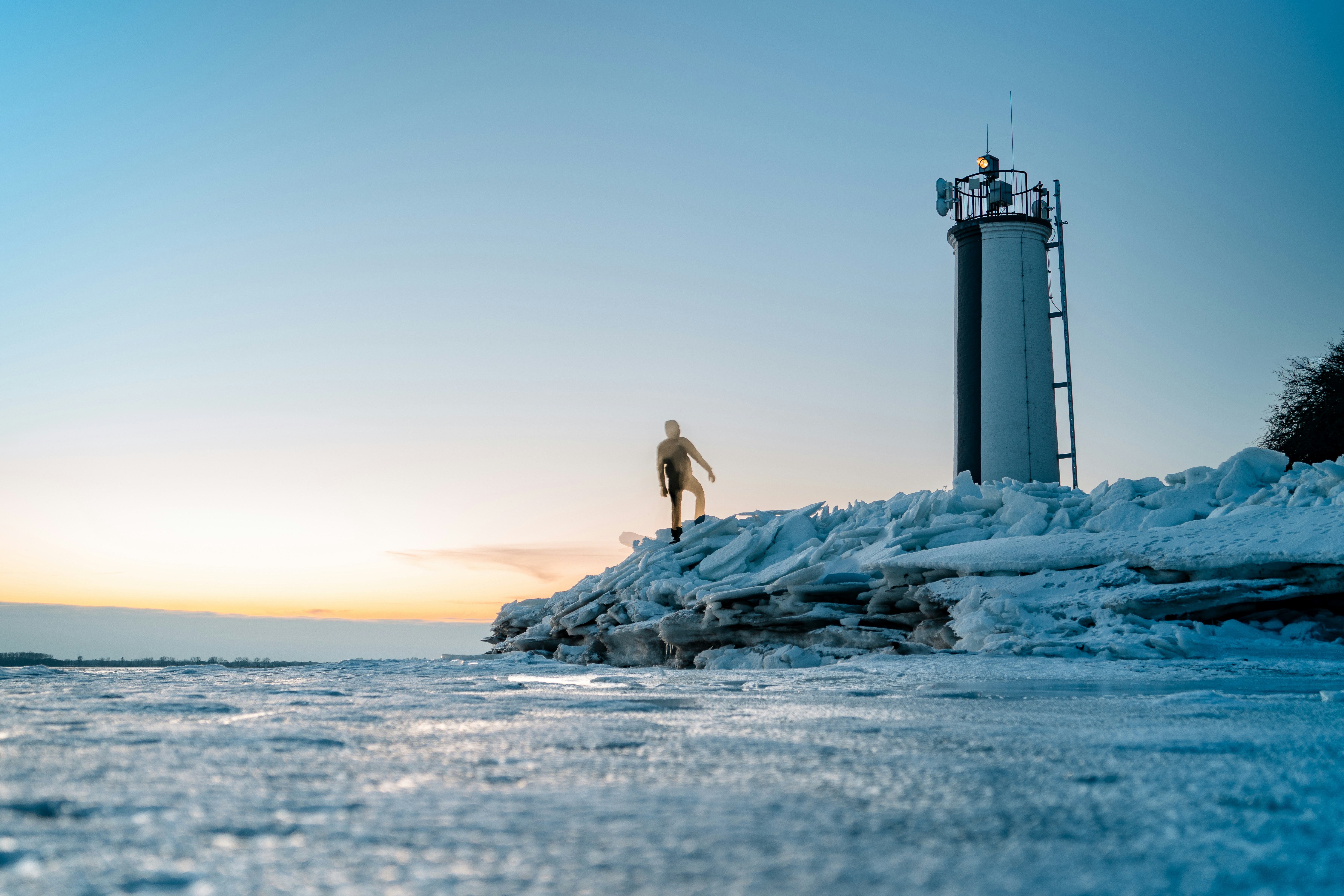 Man standing on icy shore near lighthouse at sunset