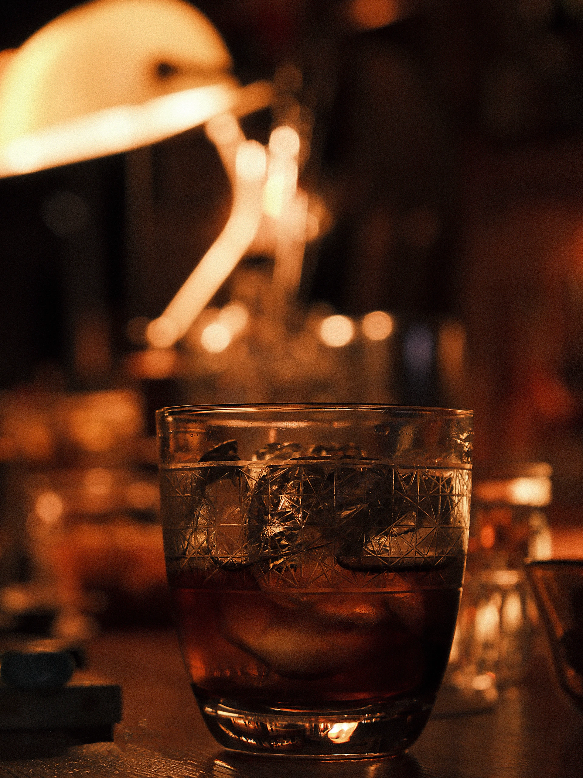 A glass of whiskey with ice on a bar counter.