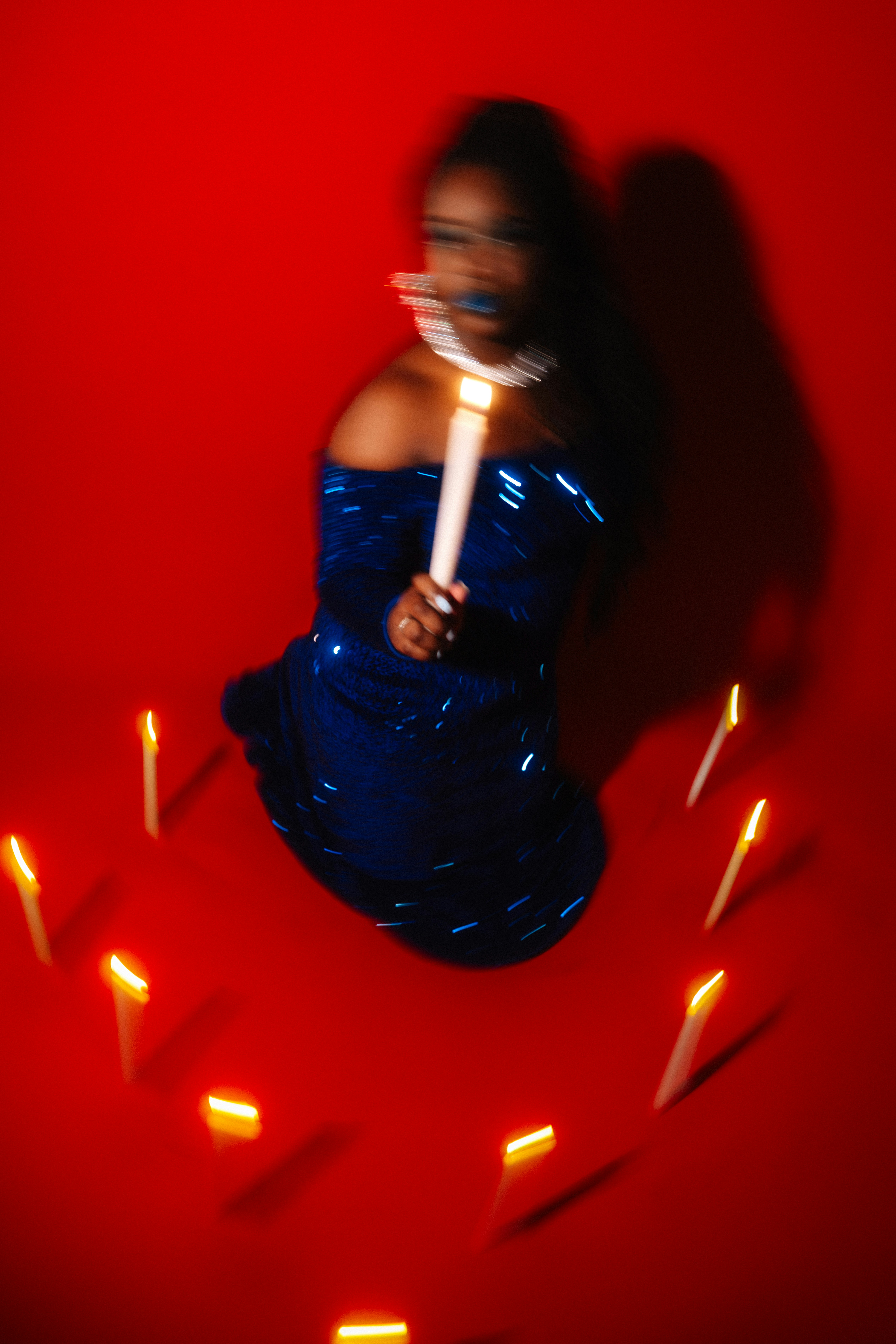 Woman in blue dress holds candle surrounded by lit candles