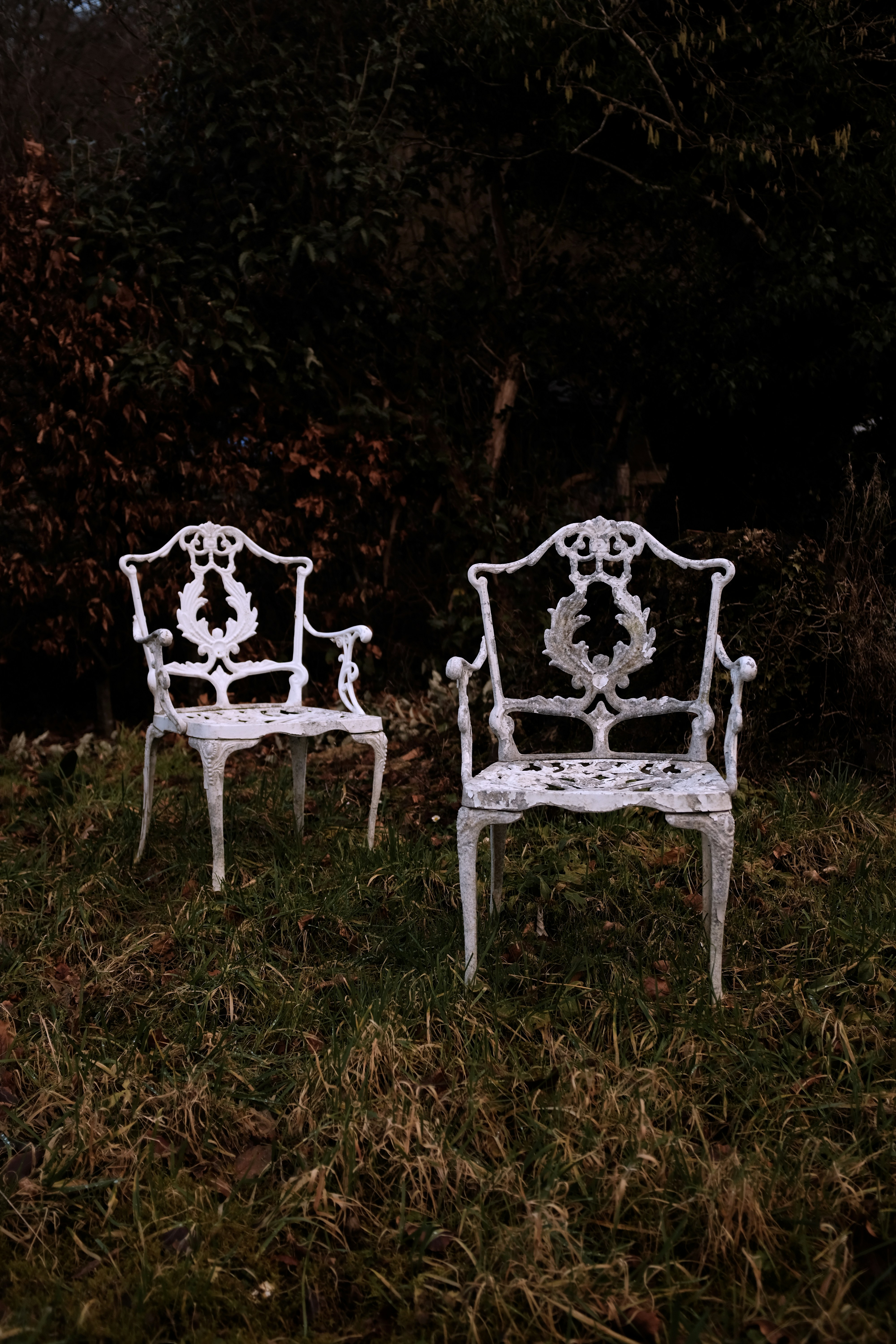 Duas cadeiras brancas ornamentadas estão em um jardim gramado.