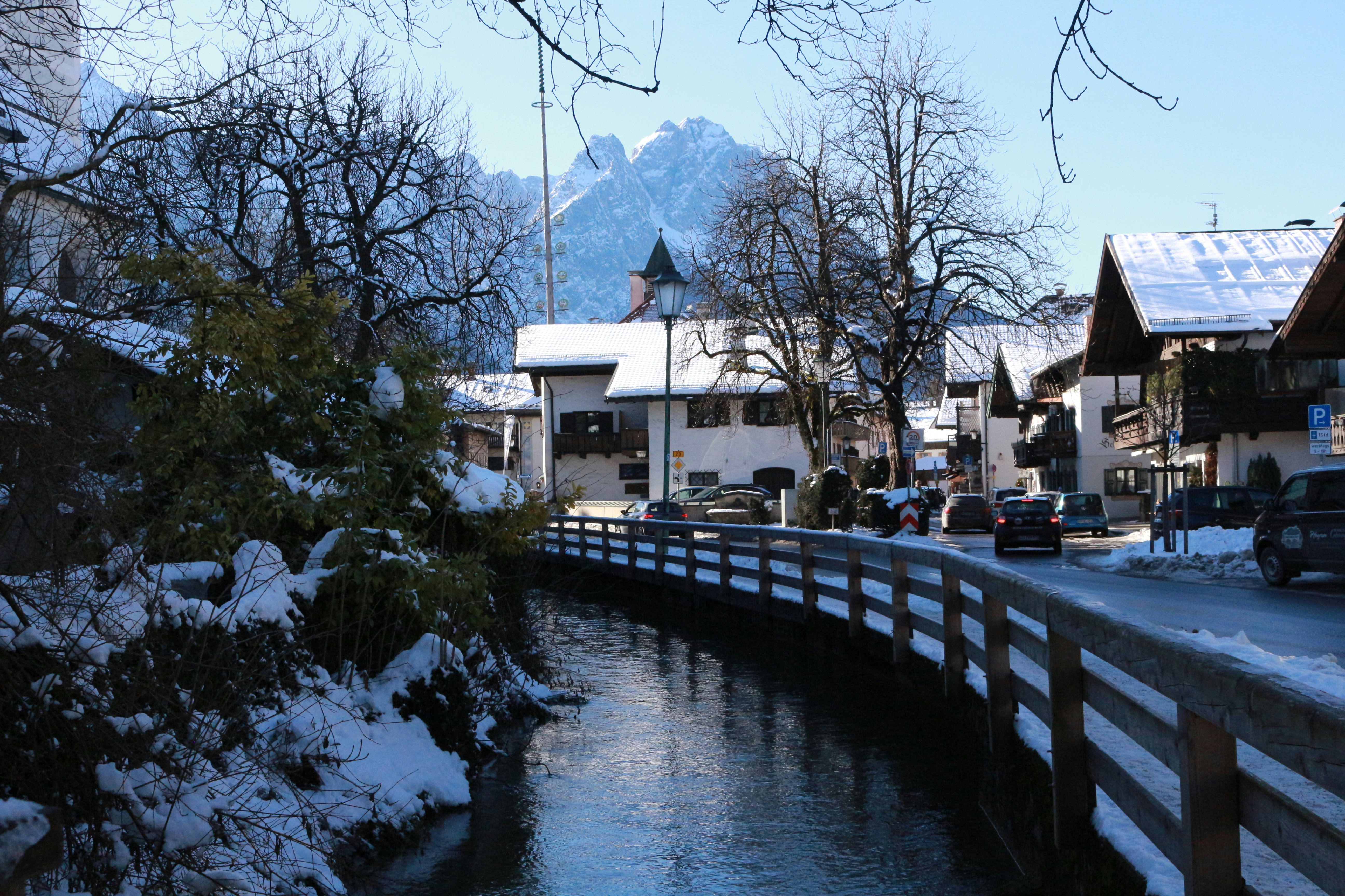 Snowy village scene with a canal and mountains.