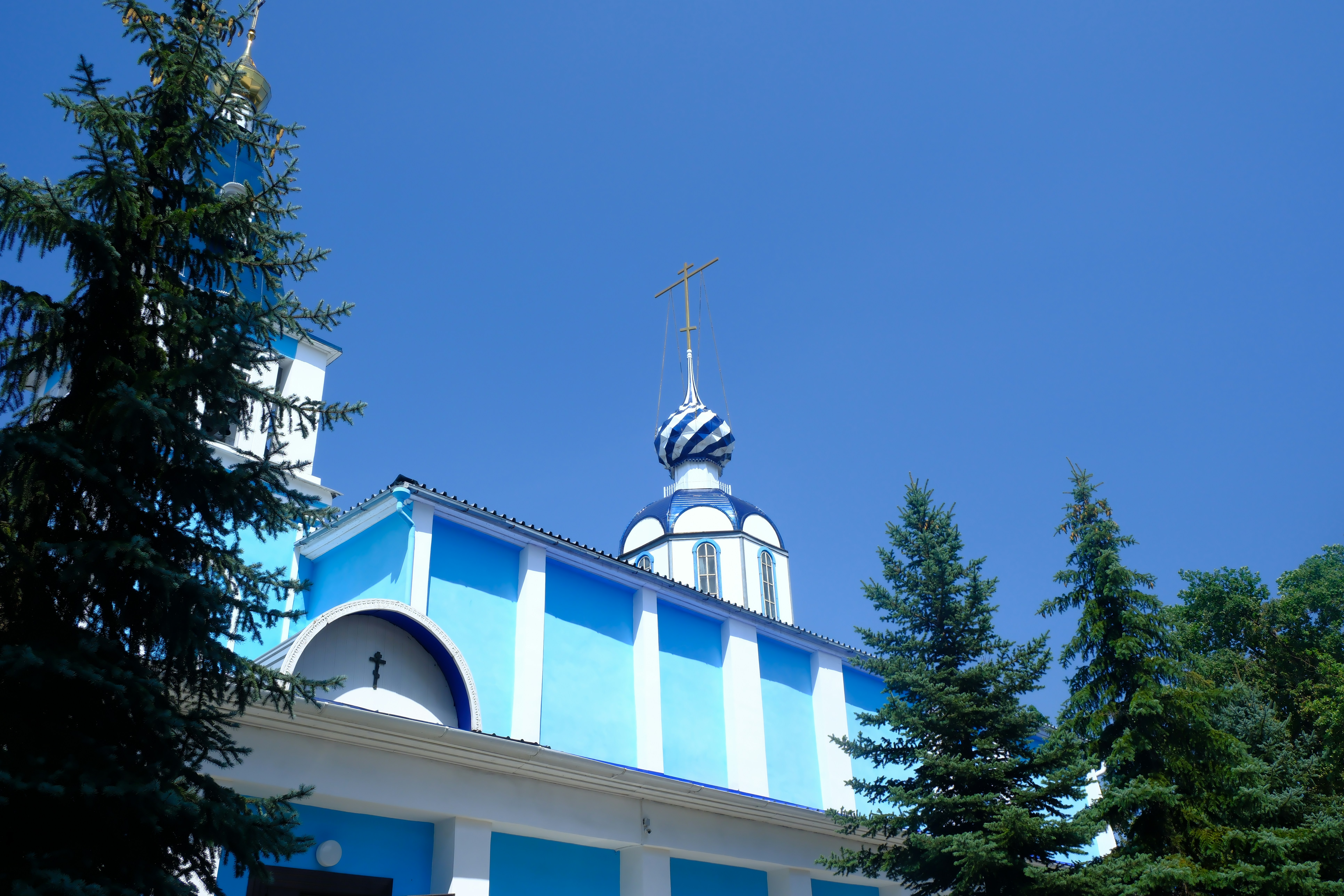 Blue and white church with pine trees and blue sky