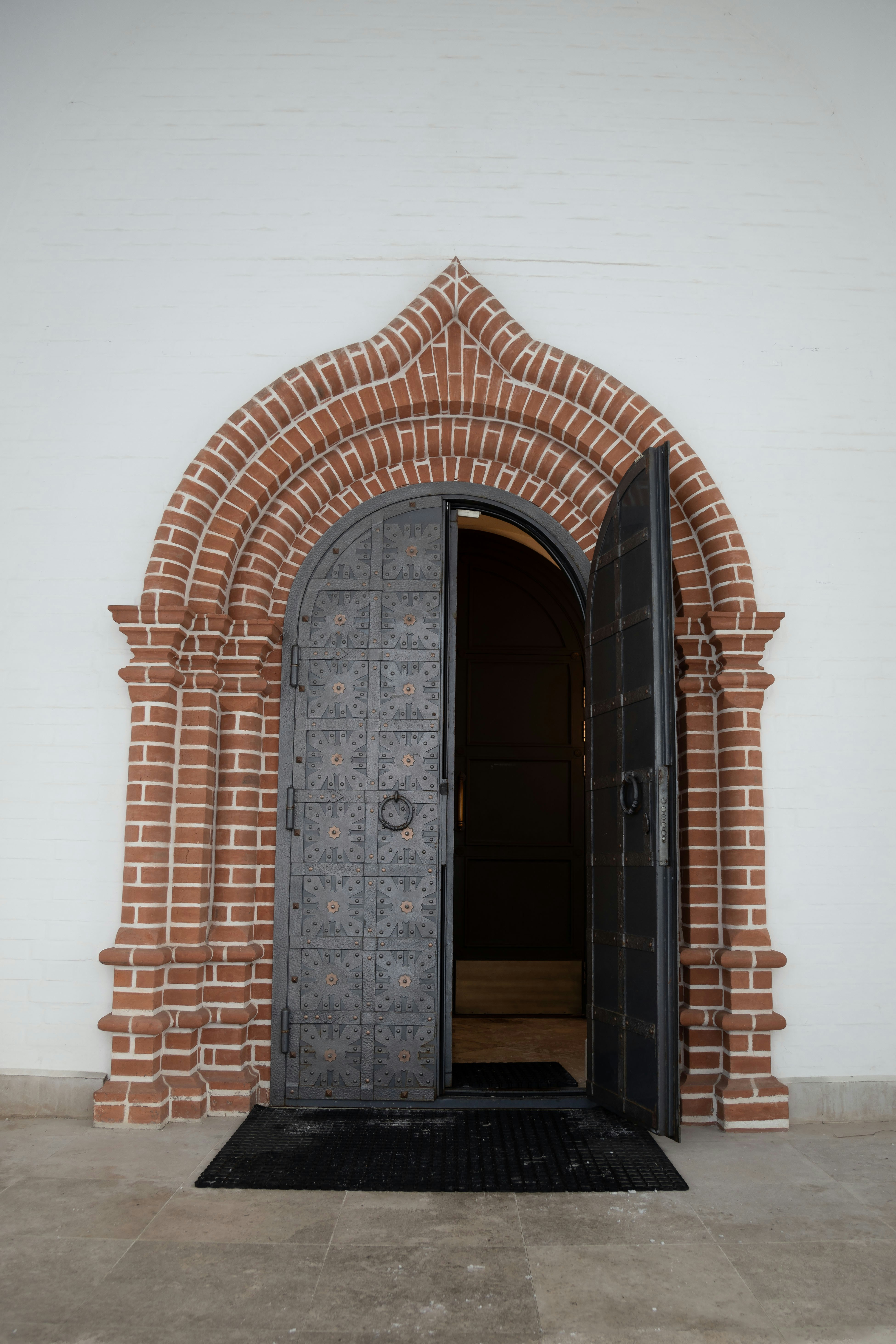 An open ornate metal door set in a brick archway