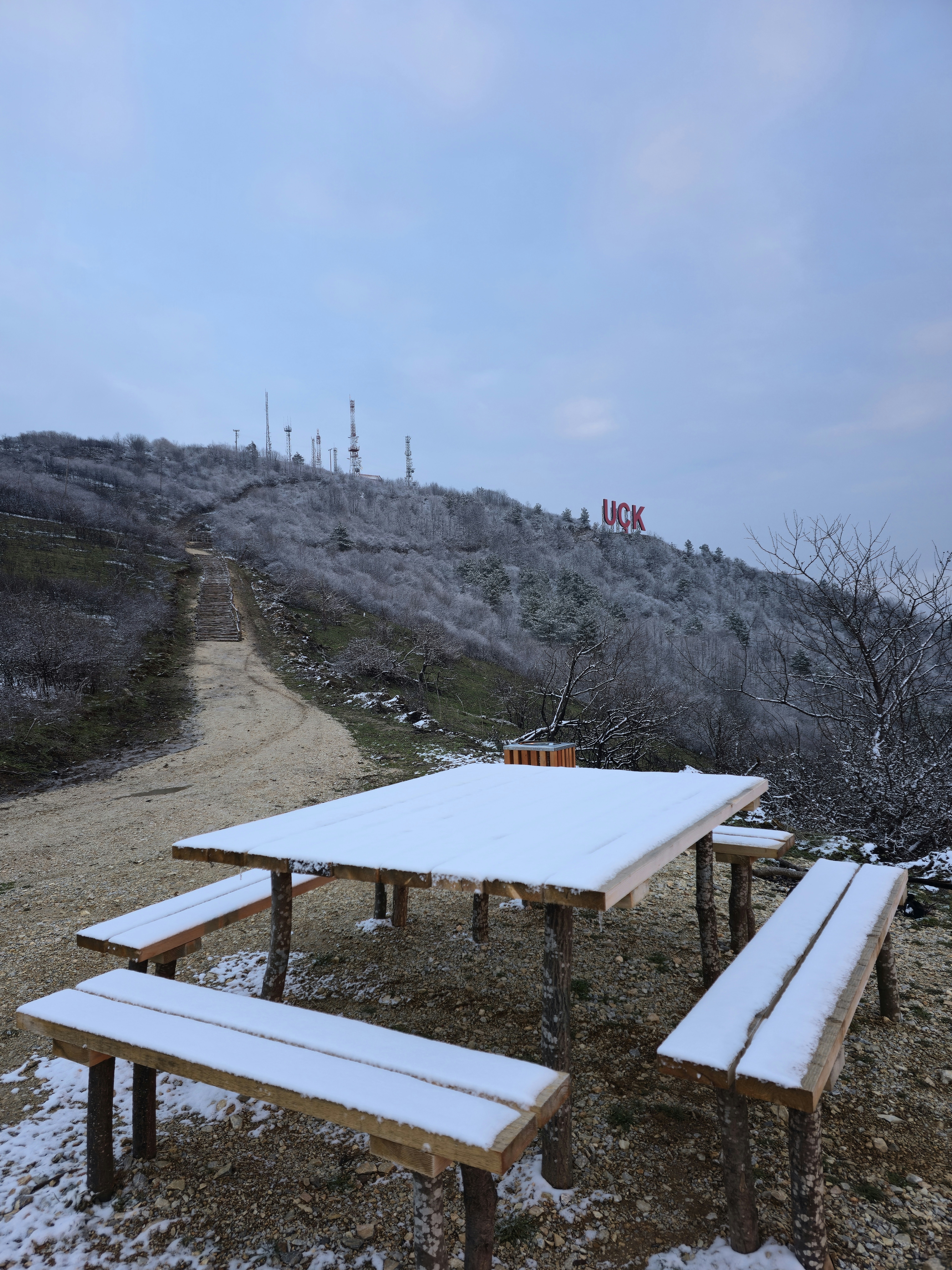 Snow-covered picnic table with uck sign on hill.