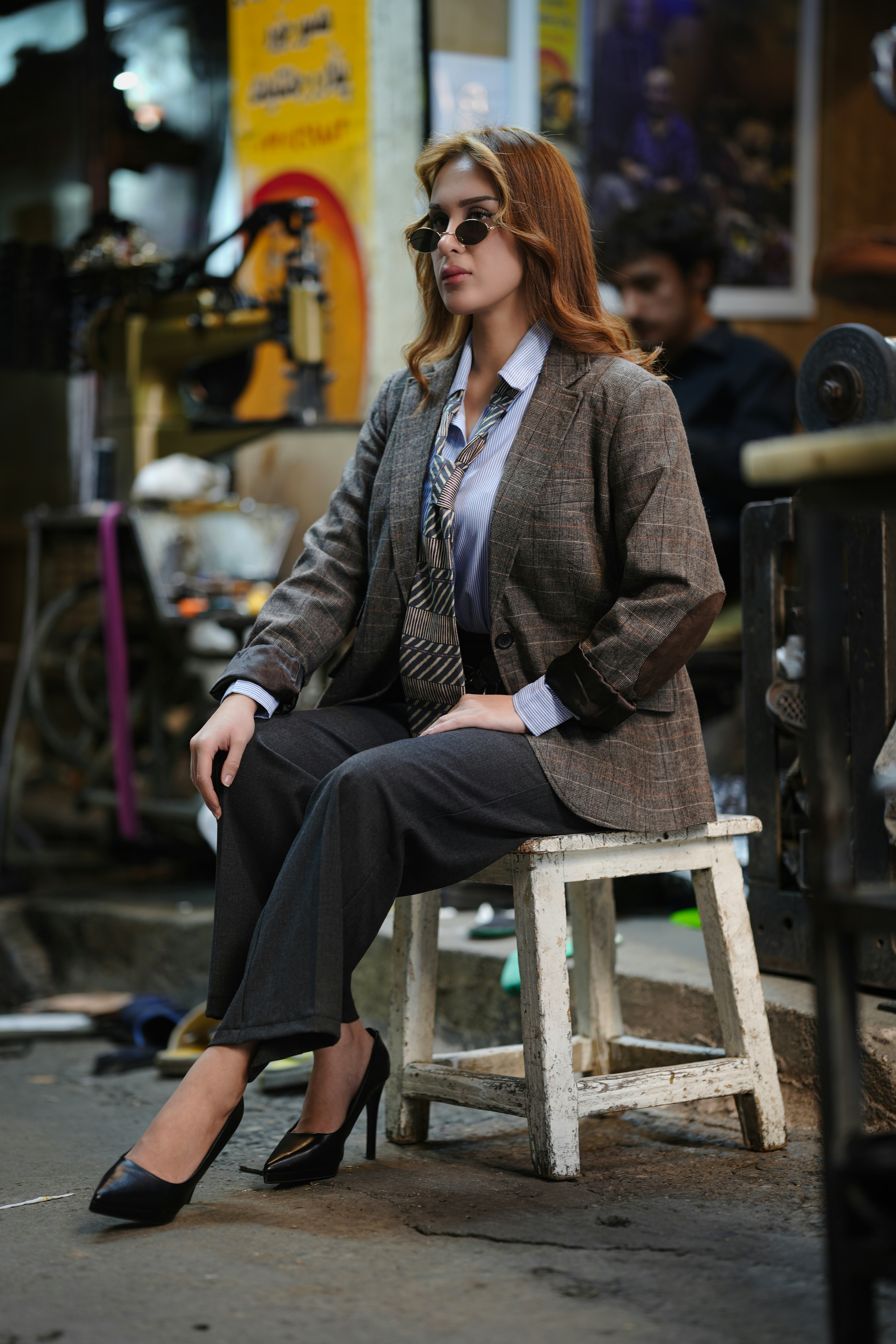 Woman in stylish outfit sitting on stool in workshop.