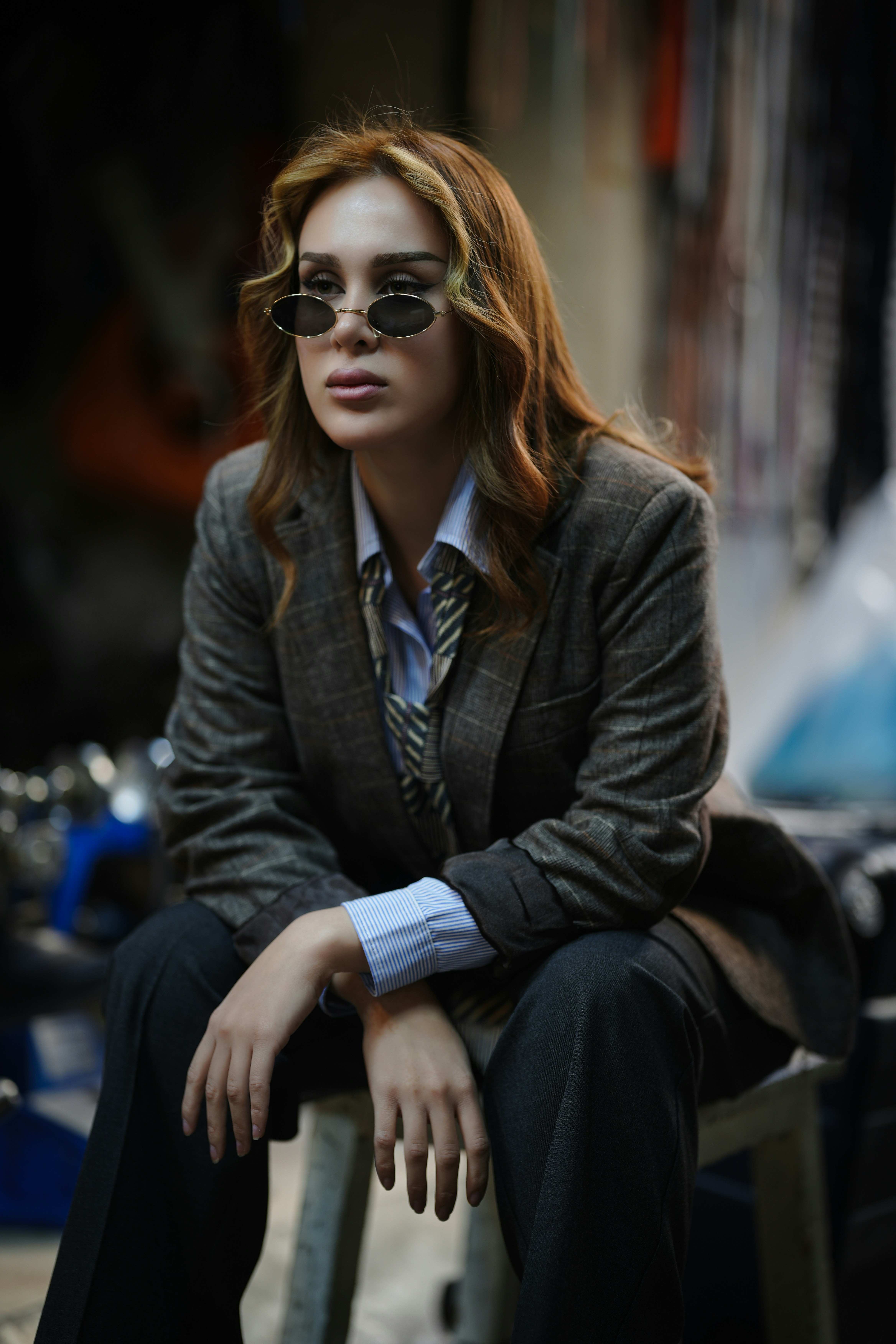 Woman in suit and sunglasses sits looking away