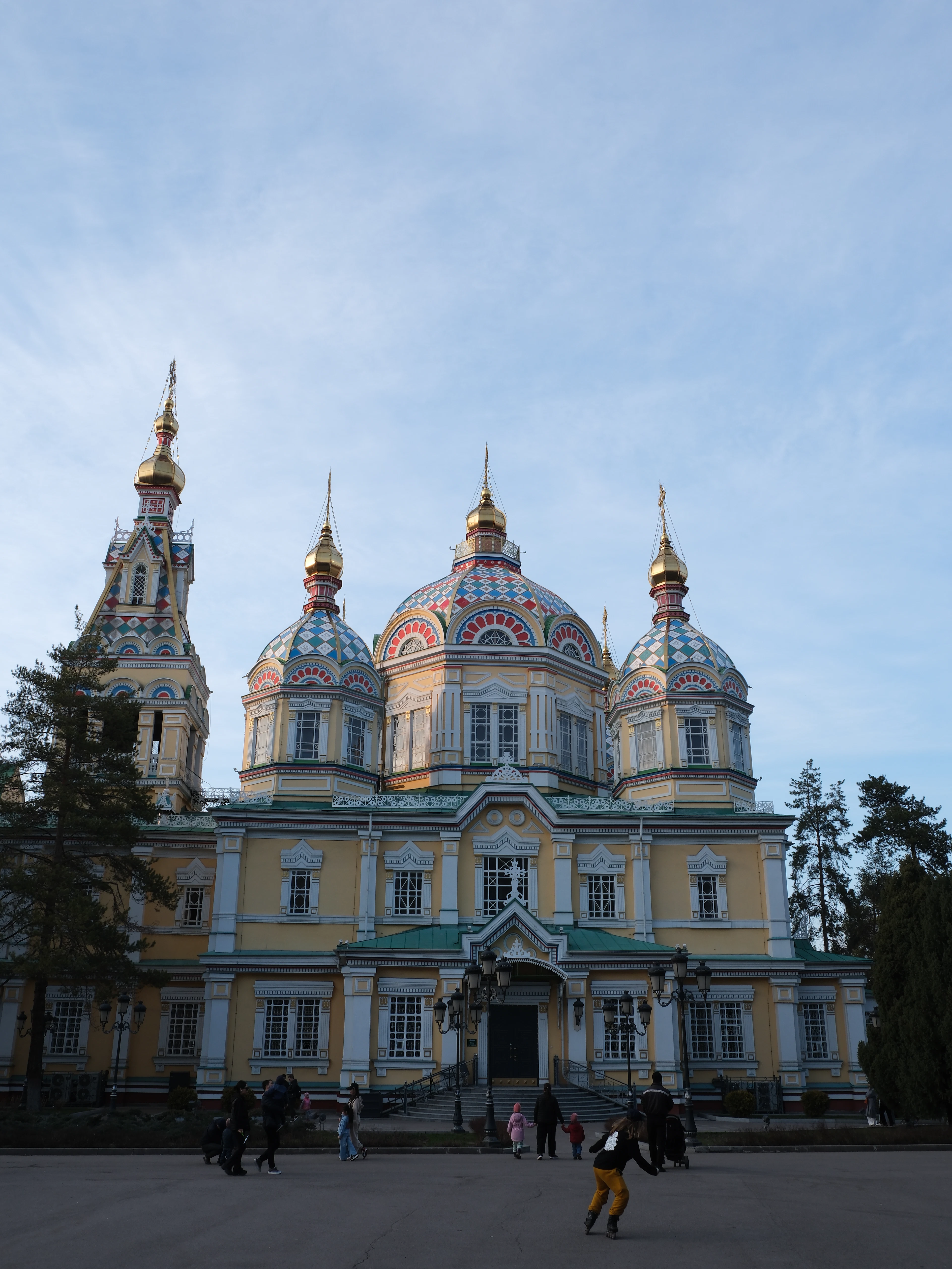 Ascension Cathedral's colorful onion domes catch golden evening light as people stroll the square in front of it.