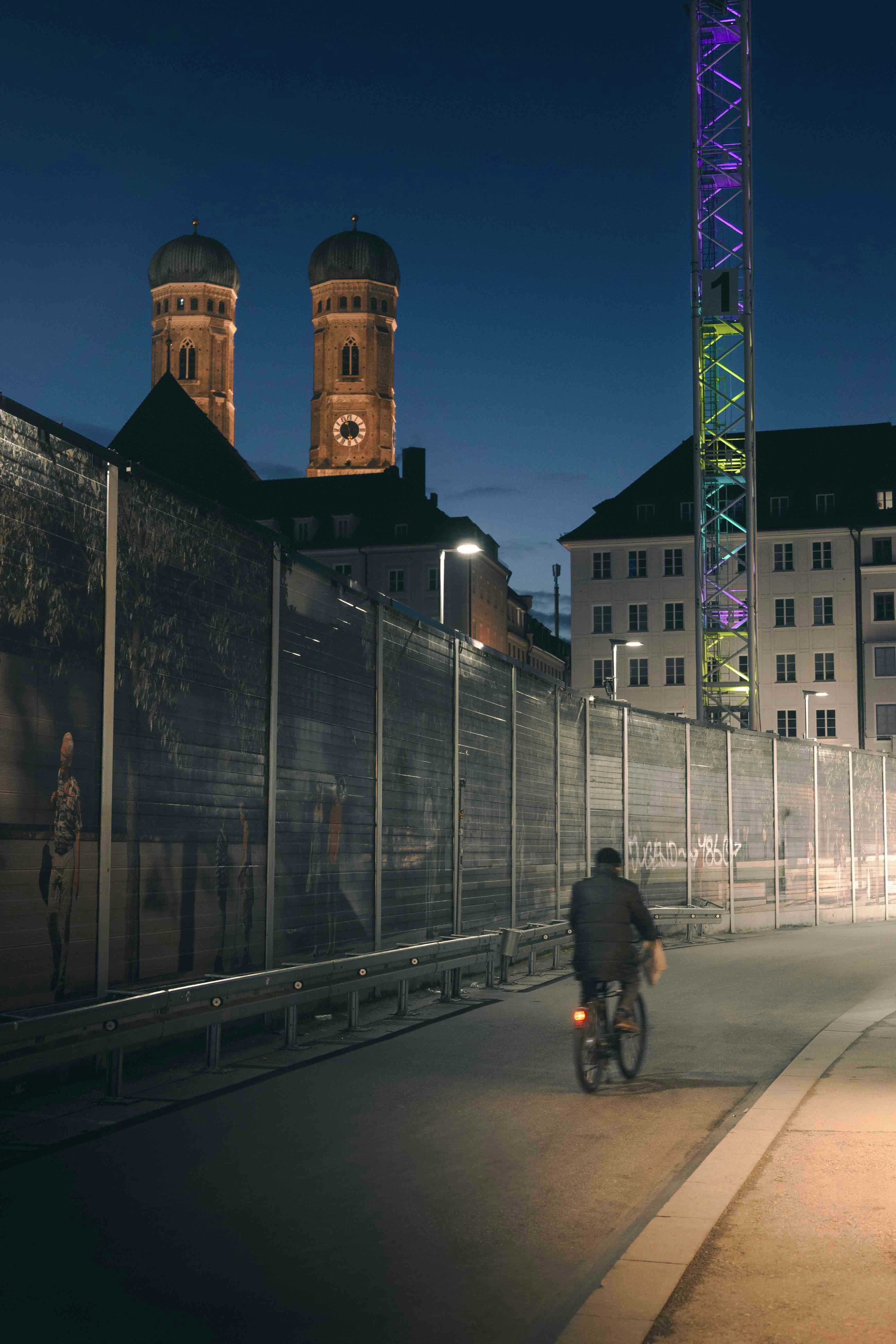 Man cycles past construction site with illuminated towers.