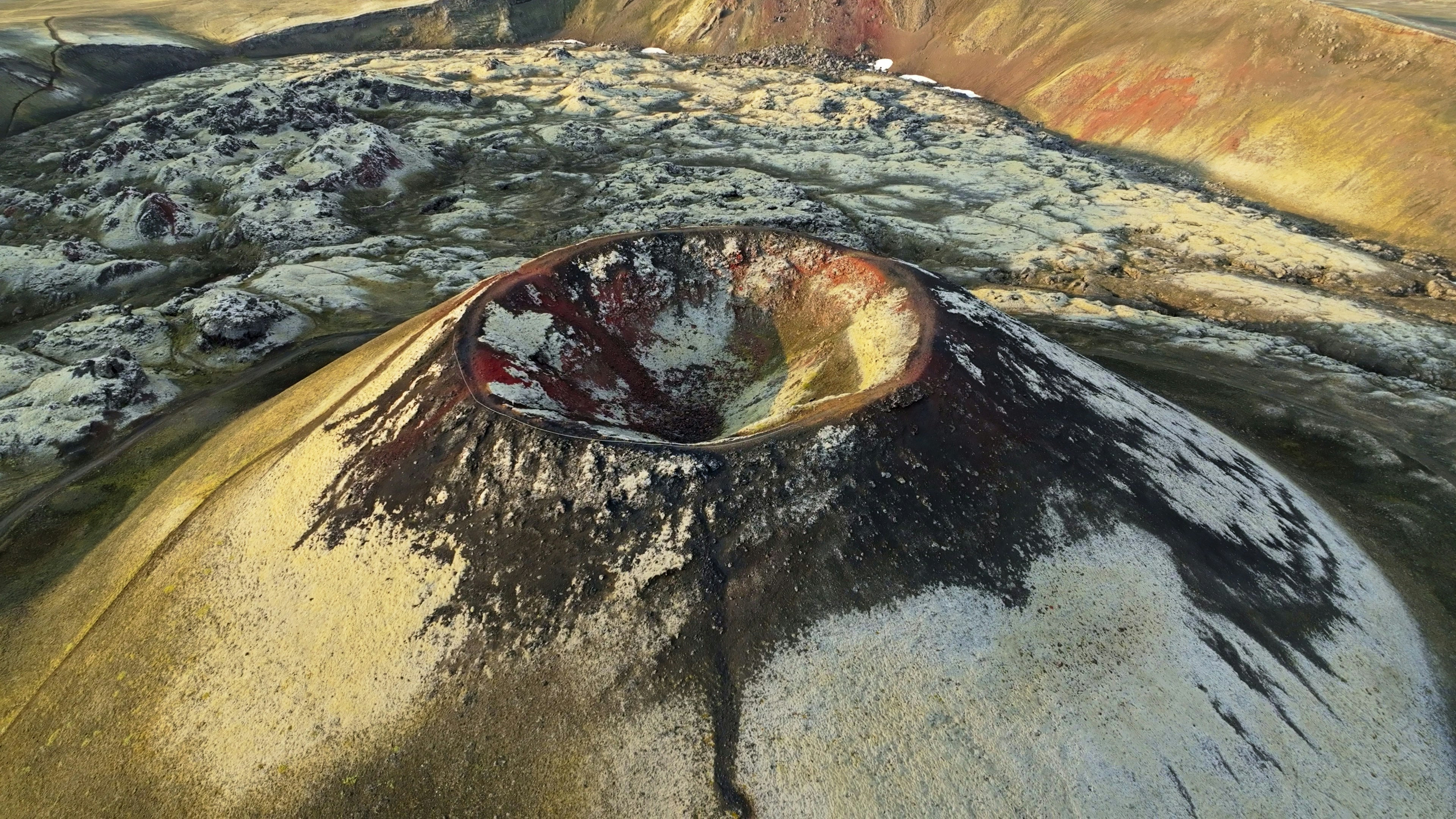 Aerial view of a volcanic crater with colorful mineral deposits.
