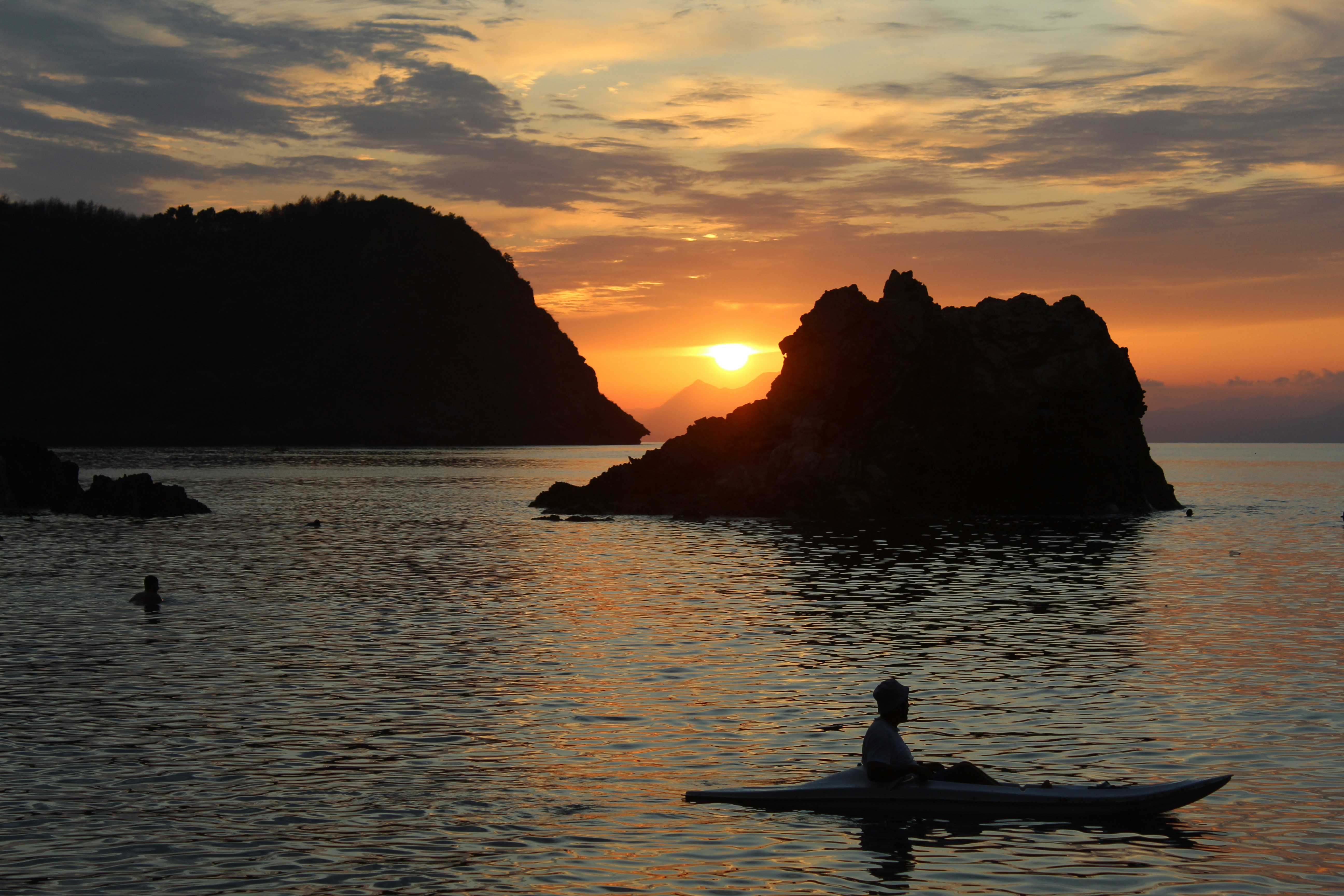 A person kayaks on the water at sunset.