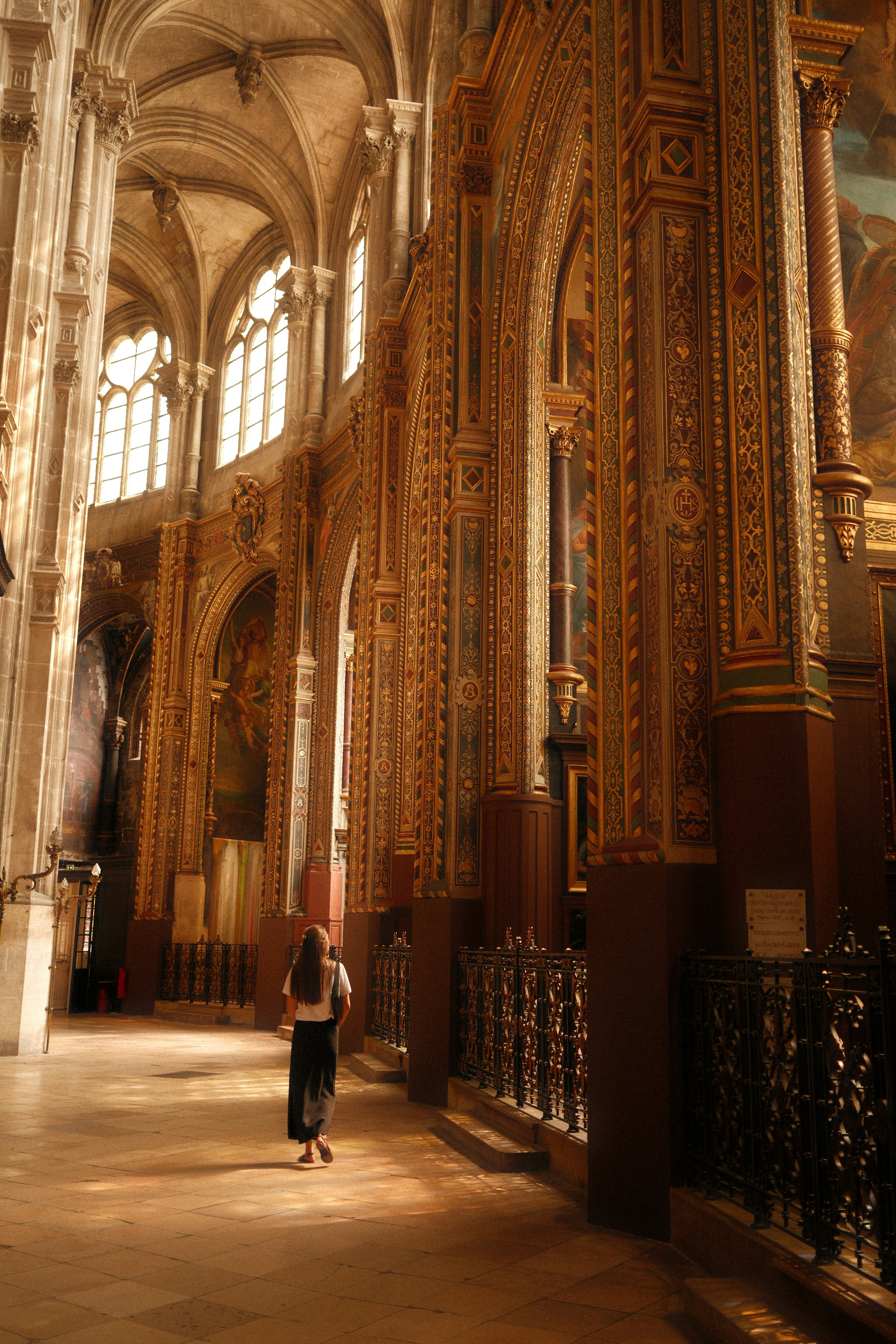 Femme marchant dans une allée ornée d’église sous le soleil.