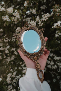 Hand holding ornate antique mirror with flowering bush background