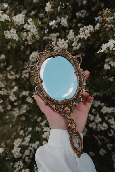 Hand holding ornate antique mirror with flowering bush background