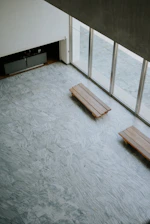 Two wooden benches on a marbled floor by large windows