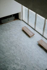 Two wooden benches on a marbled floor by large windows