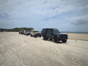 Several 4x4 vehicles parked on a sandy beach.
