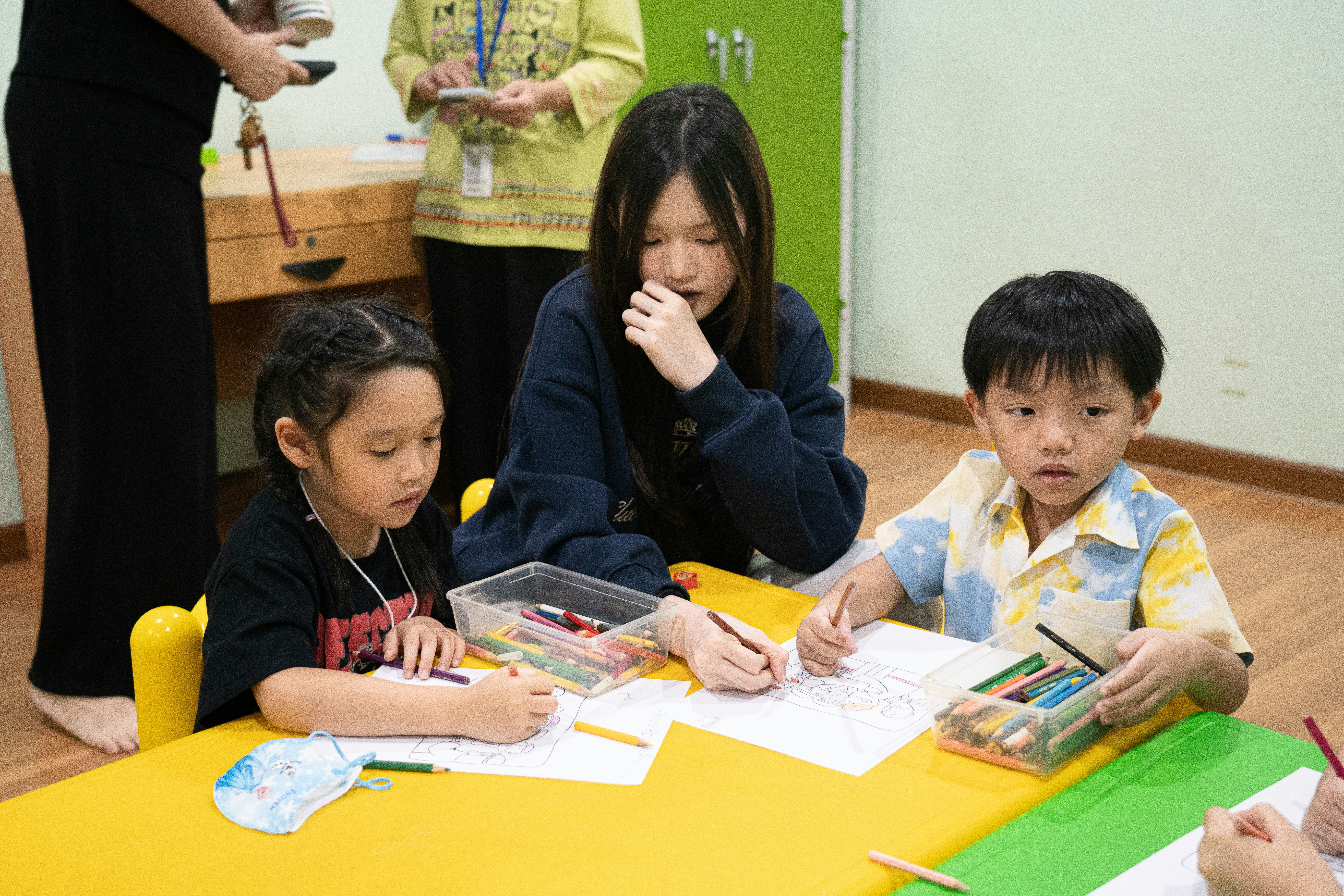 Children drawing with a teacher at a table.