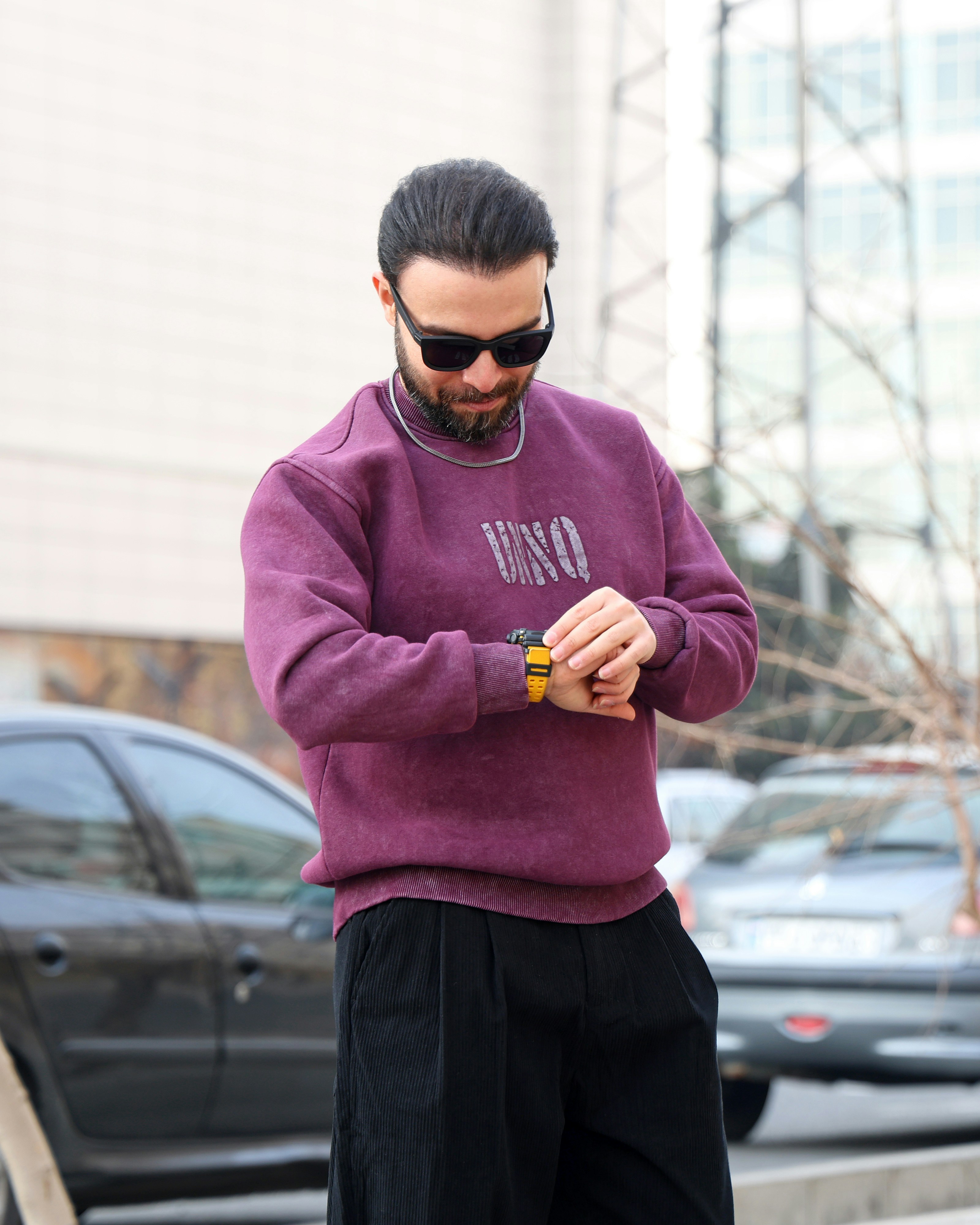 Man in sunglasses checks his watch outdoors.