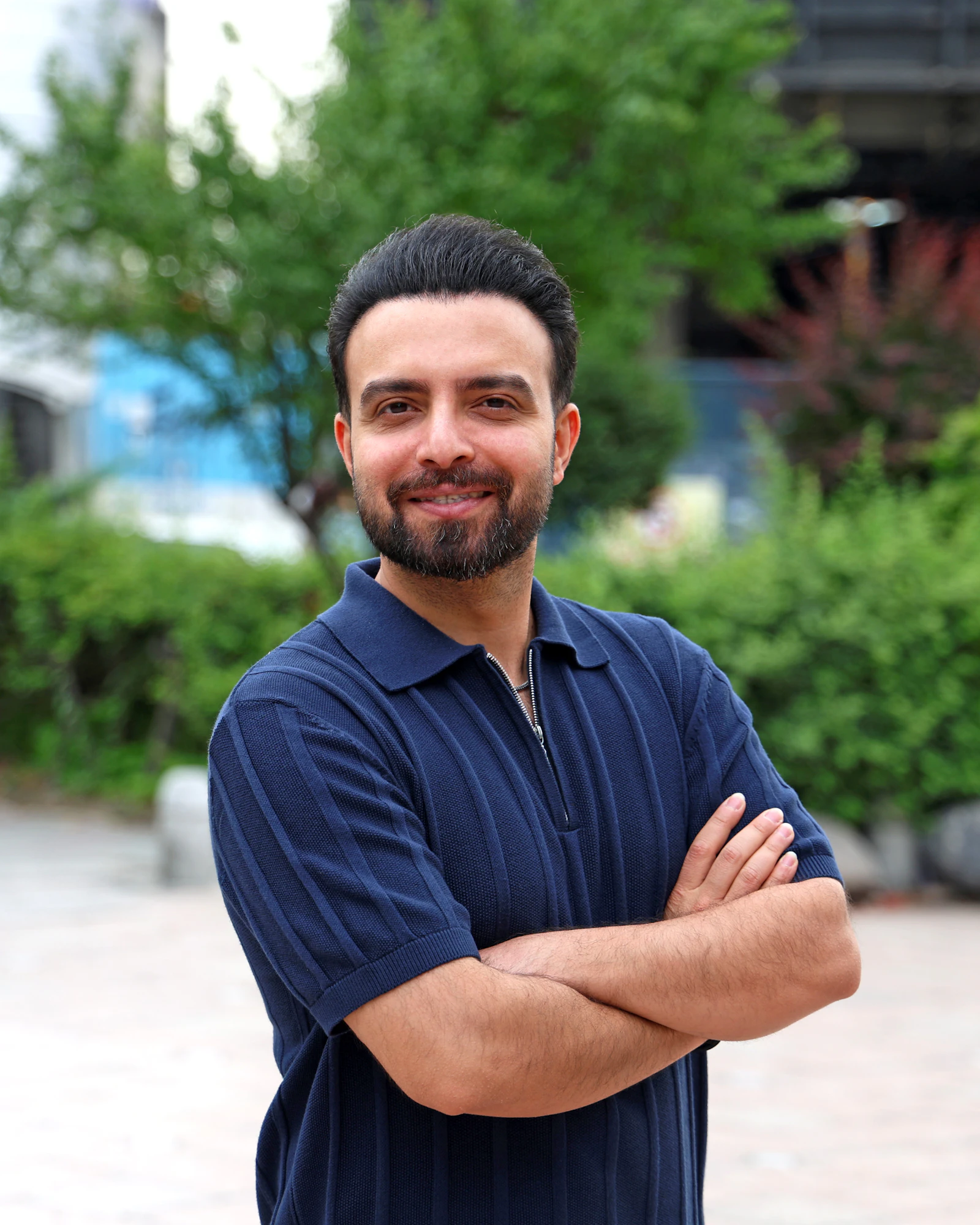 A smiling young man with his arms crossed, standing outdoors