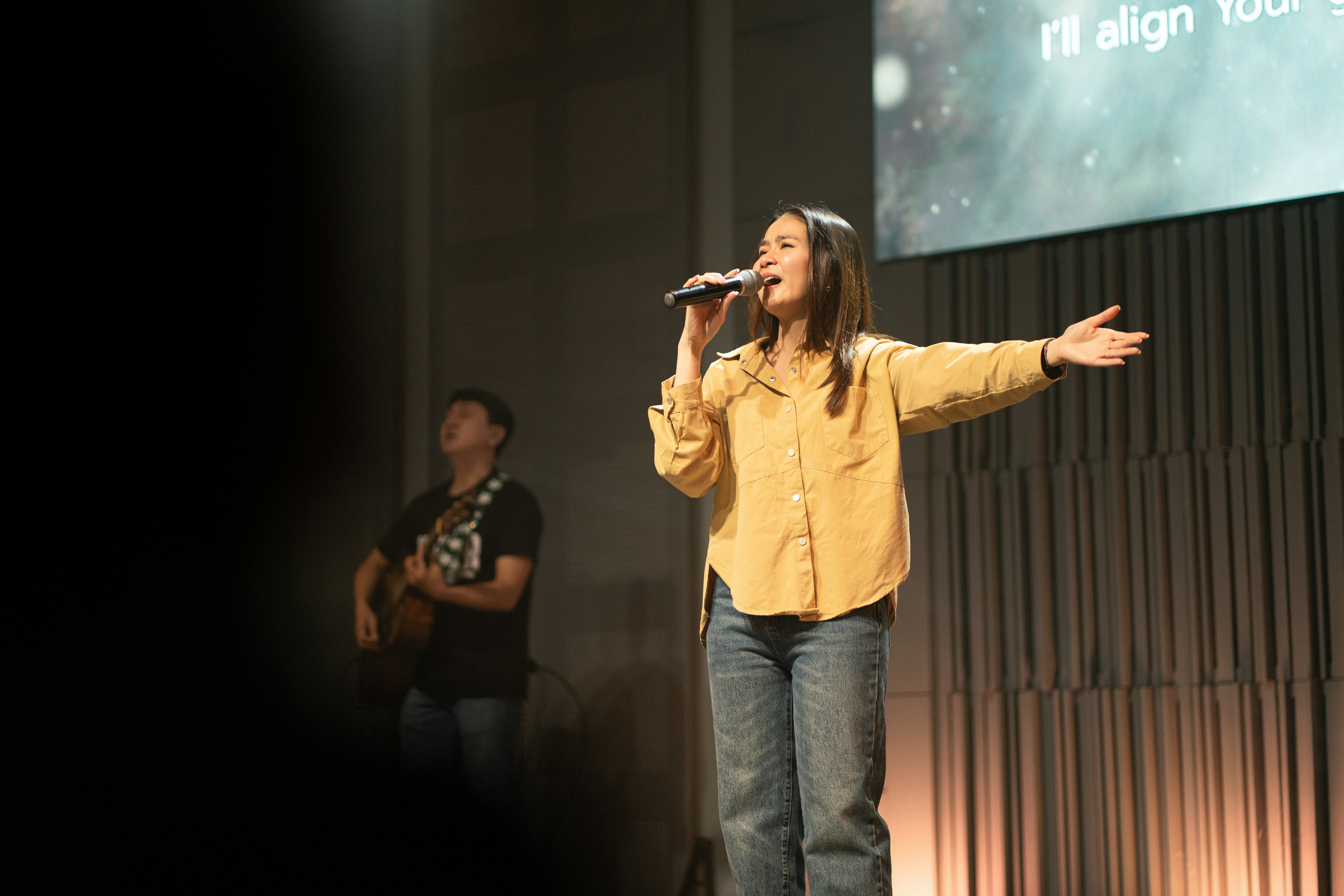 Woman singing on stage with man playing guitar.
